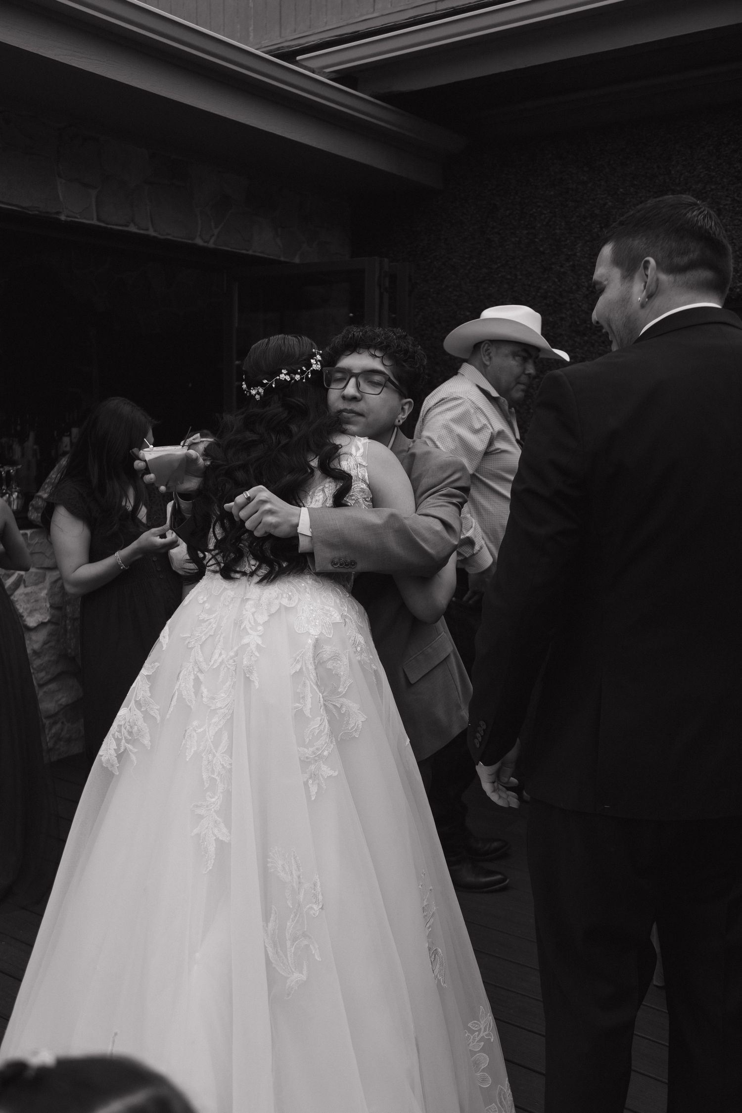 Bride in white lace gown shares first dance with guest in black and white wedding reception photo.