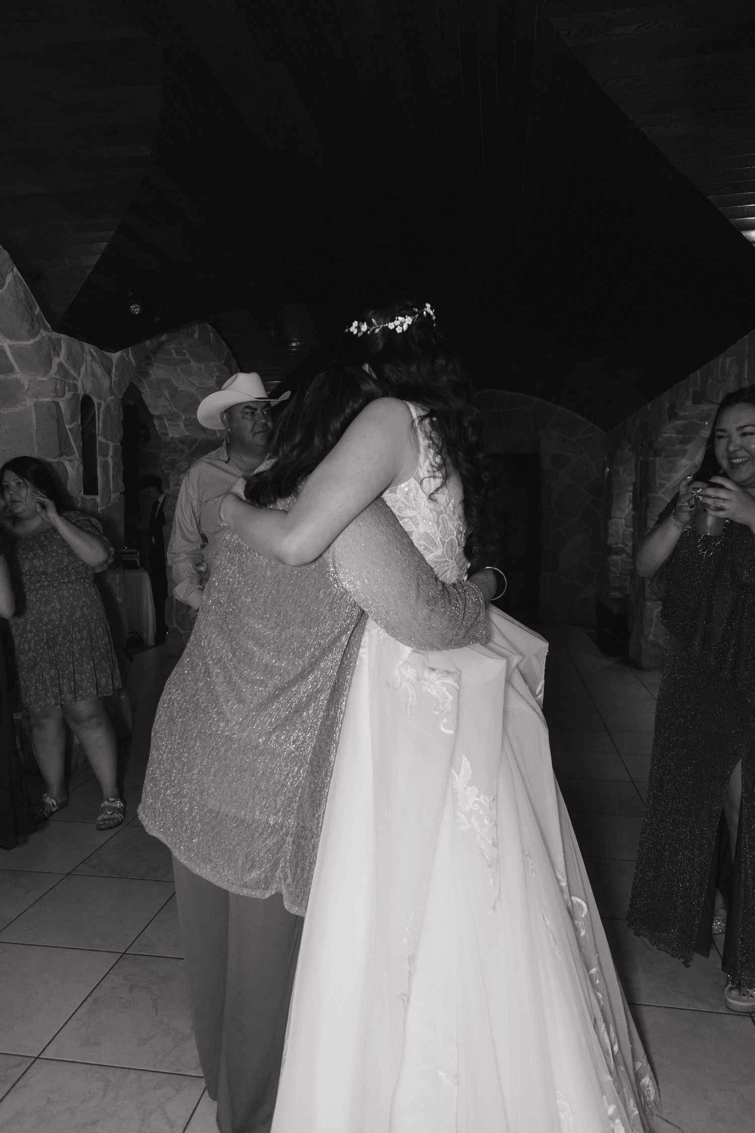 Bride in white gown shares an emotional dance with a guest in a black and white wedding photo.