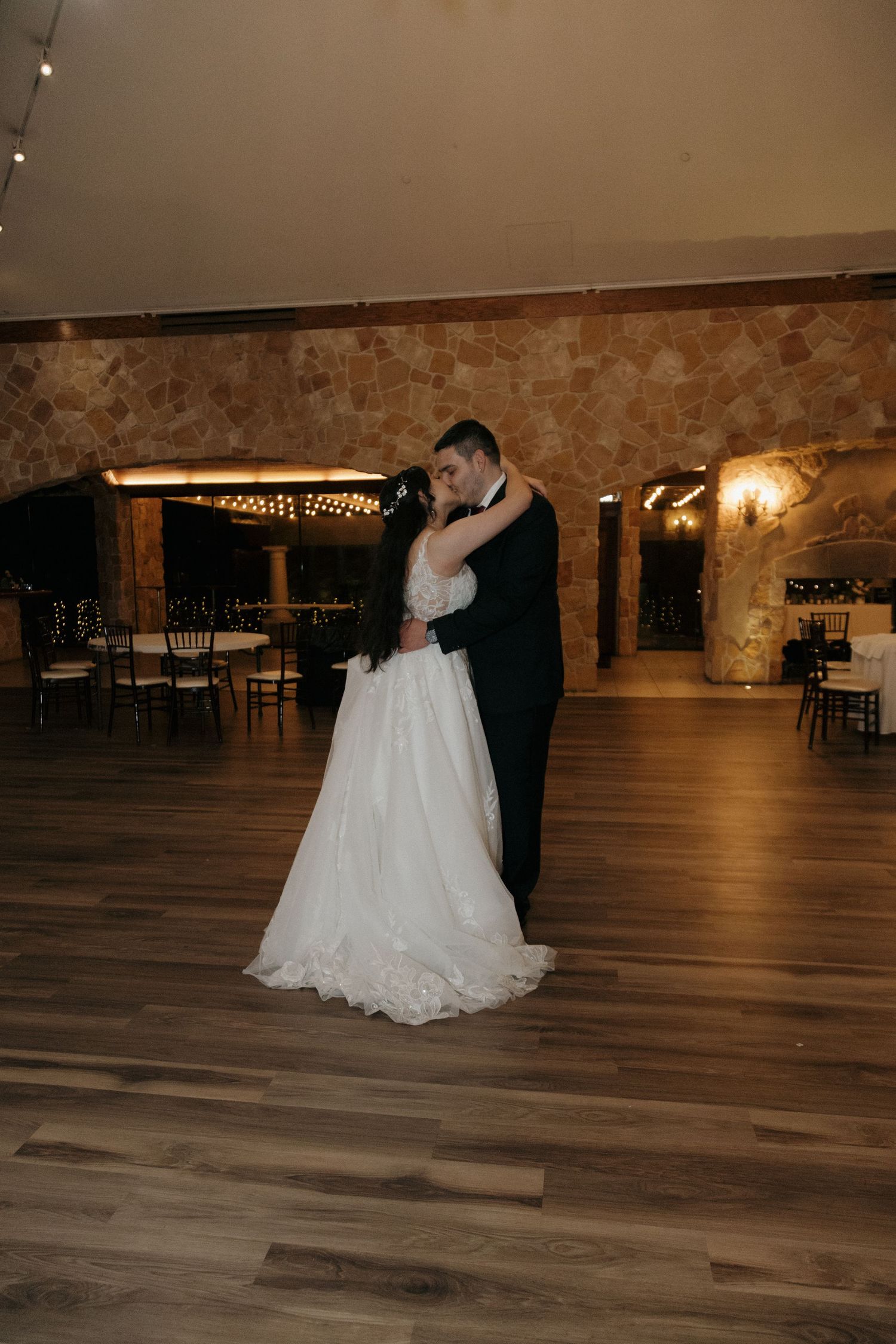 Bride and groom share an intimate first dance embrace in a rustic stone-walled wedding reception venue.