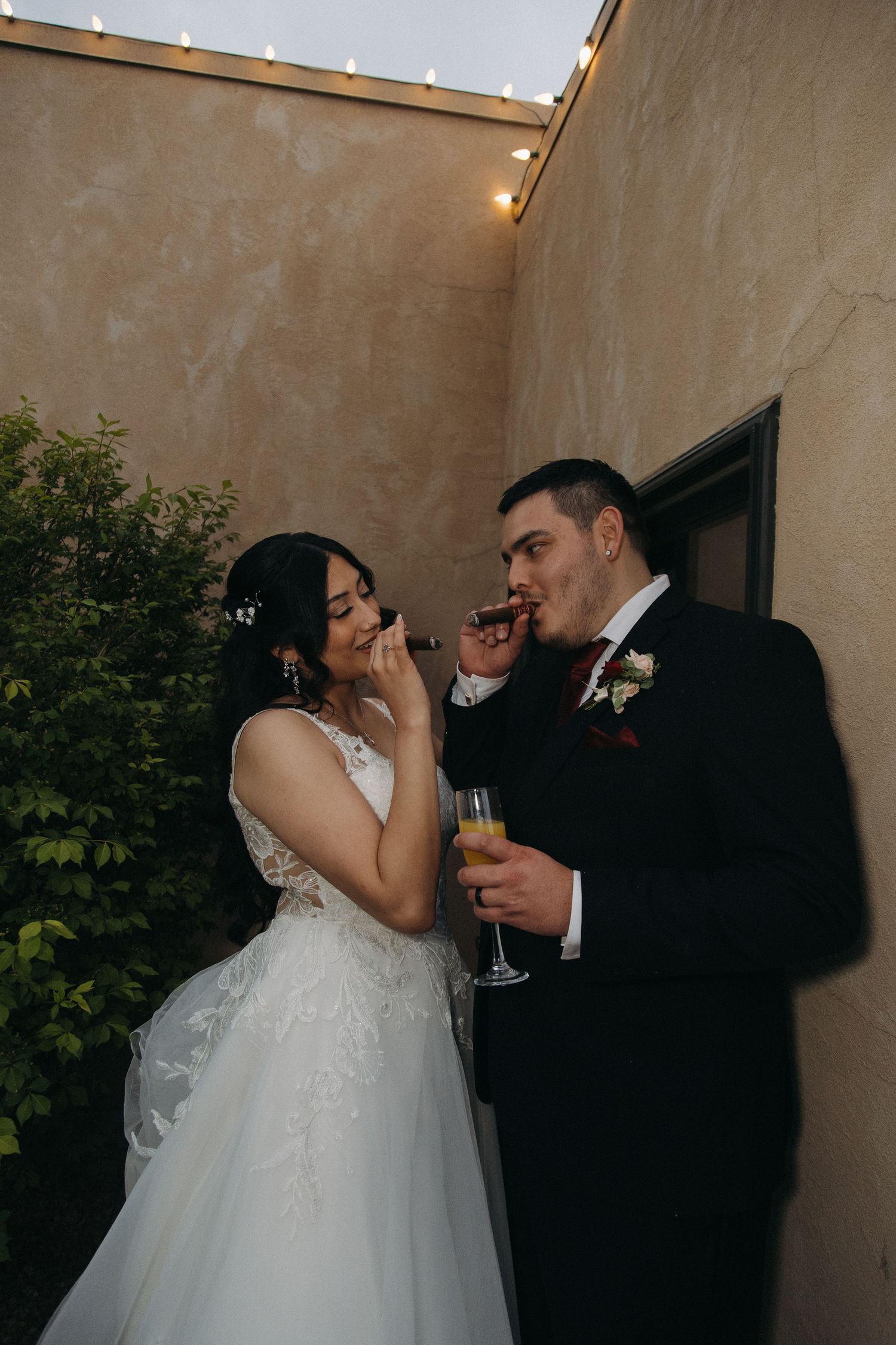 Bride and groom sharing a romantic moment with champagne and cigar at their evening wedding reception.