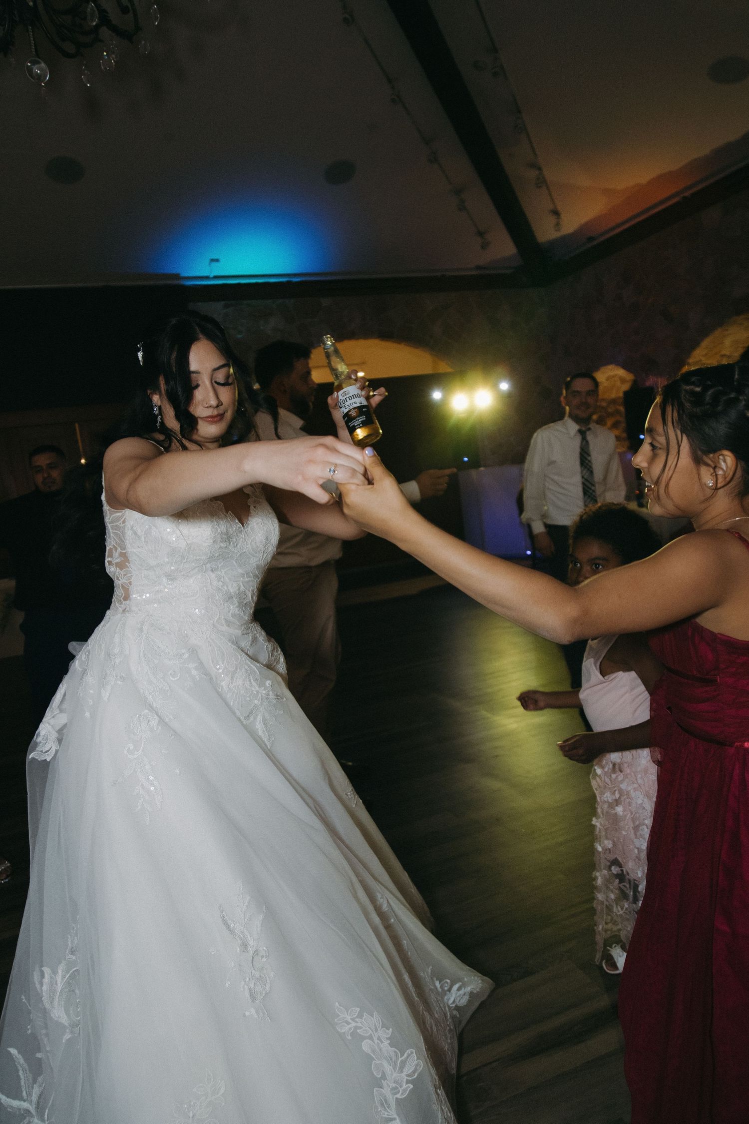 Bride in white gown dances and toasts with a beer bottle at lively wedding reception.