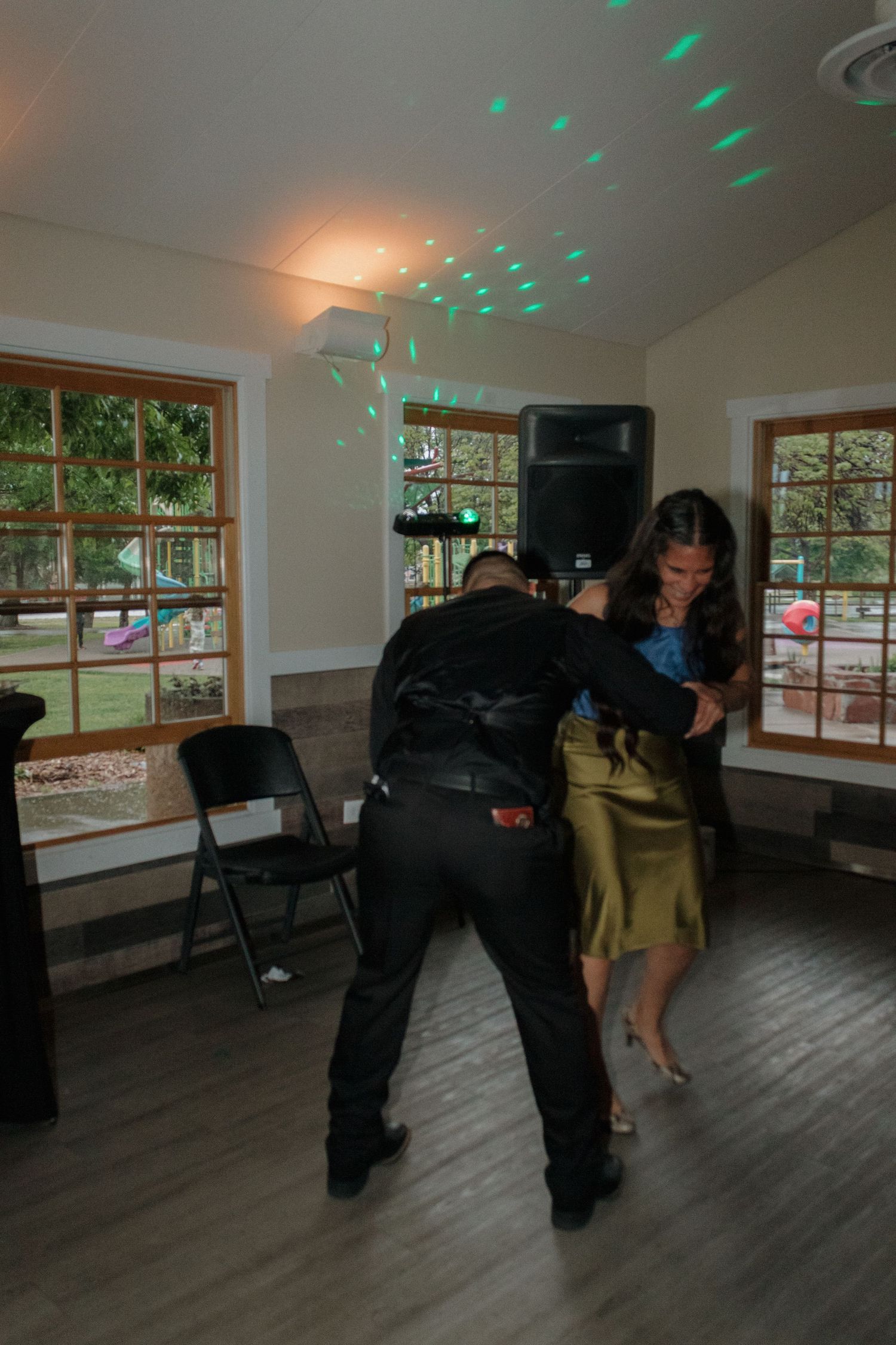 People dancing energetically in a room with green party lights and wooden floors.