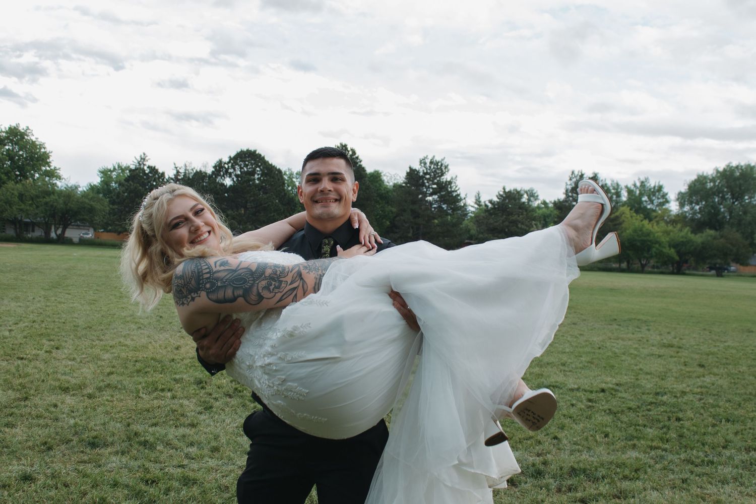 Romantic dancing pose performed in wedding attire on grassy field.