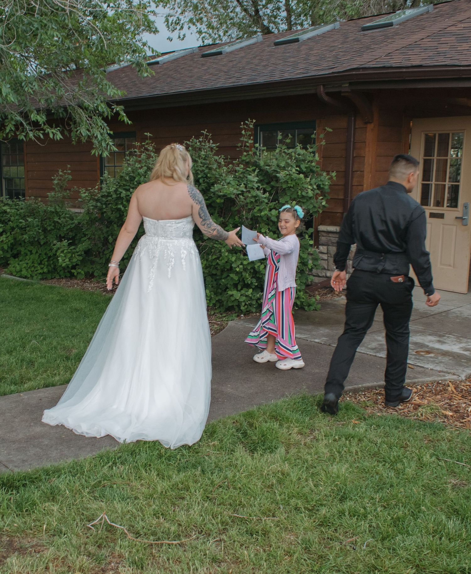 Wedding couple posing on lawn with house in background during outdoor celebration.