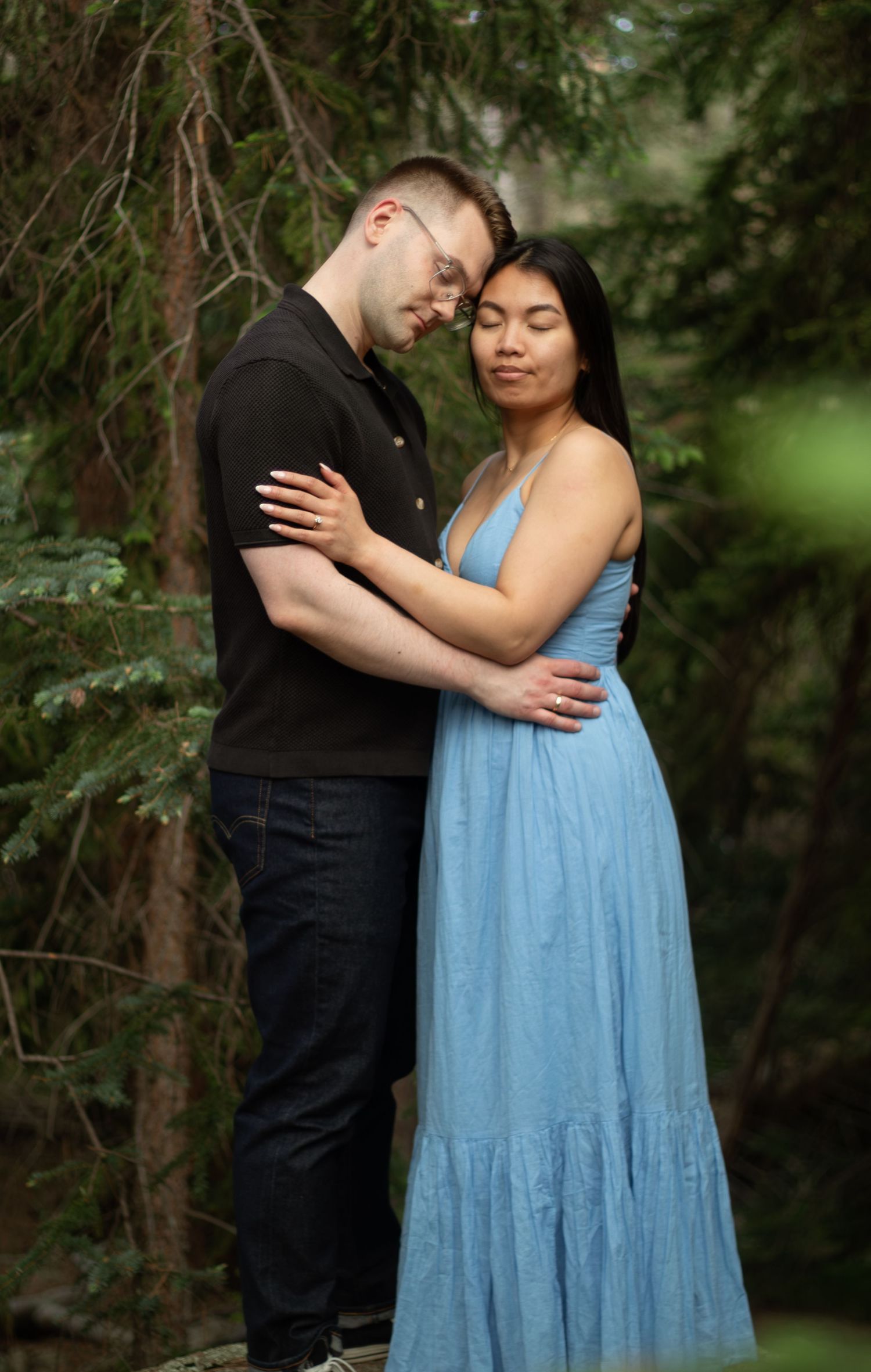 A tender moment between two people wearing formal attire in a lush forest setting.
