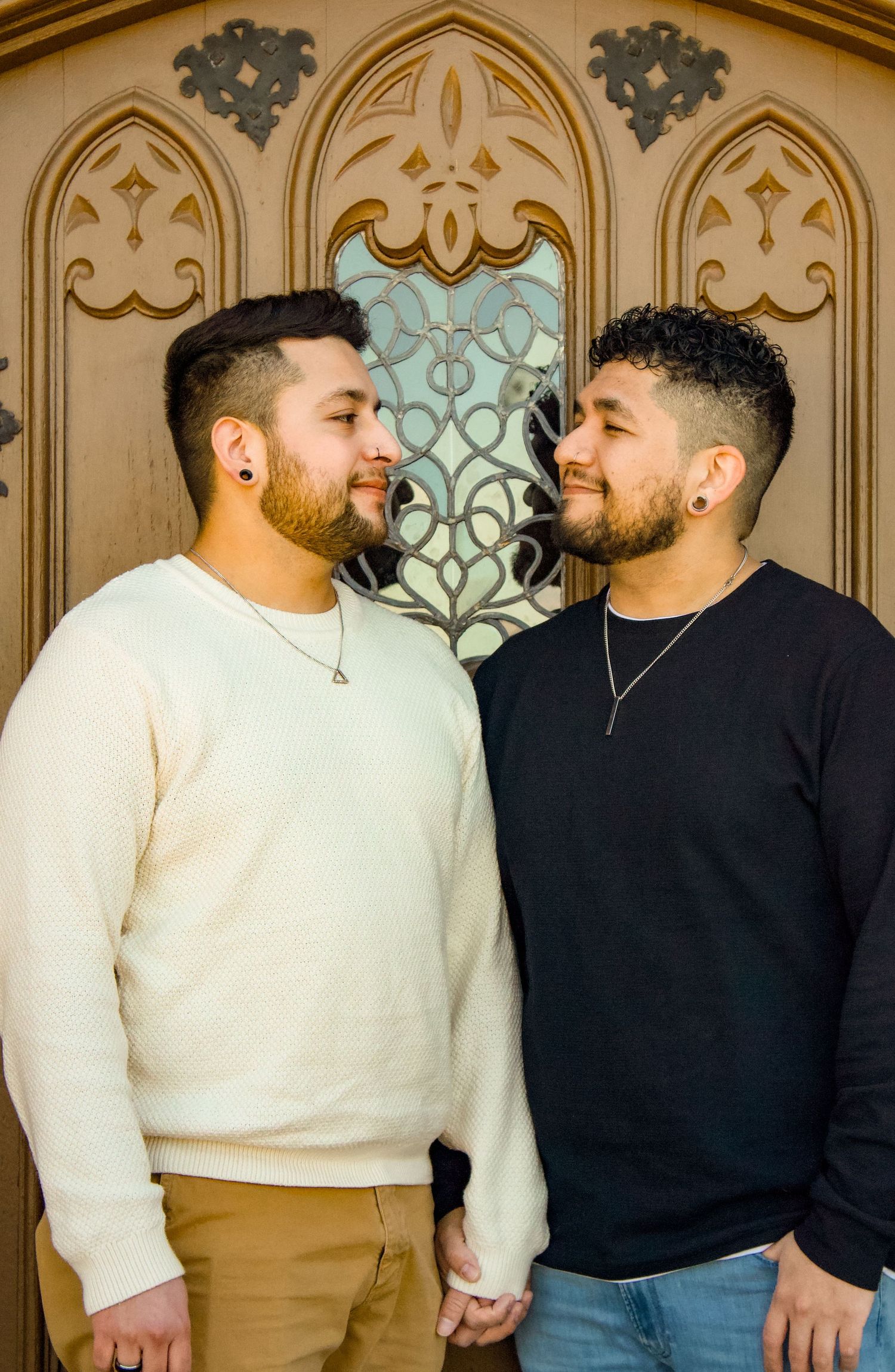 Two people in contrasting sweaters sharing a tender moment against an ornate architectural backdrop.