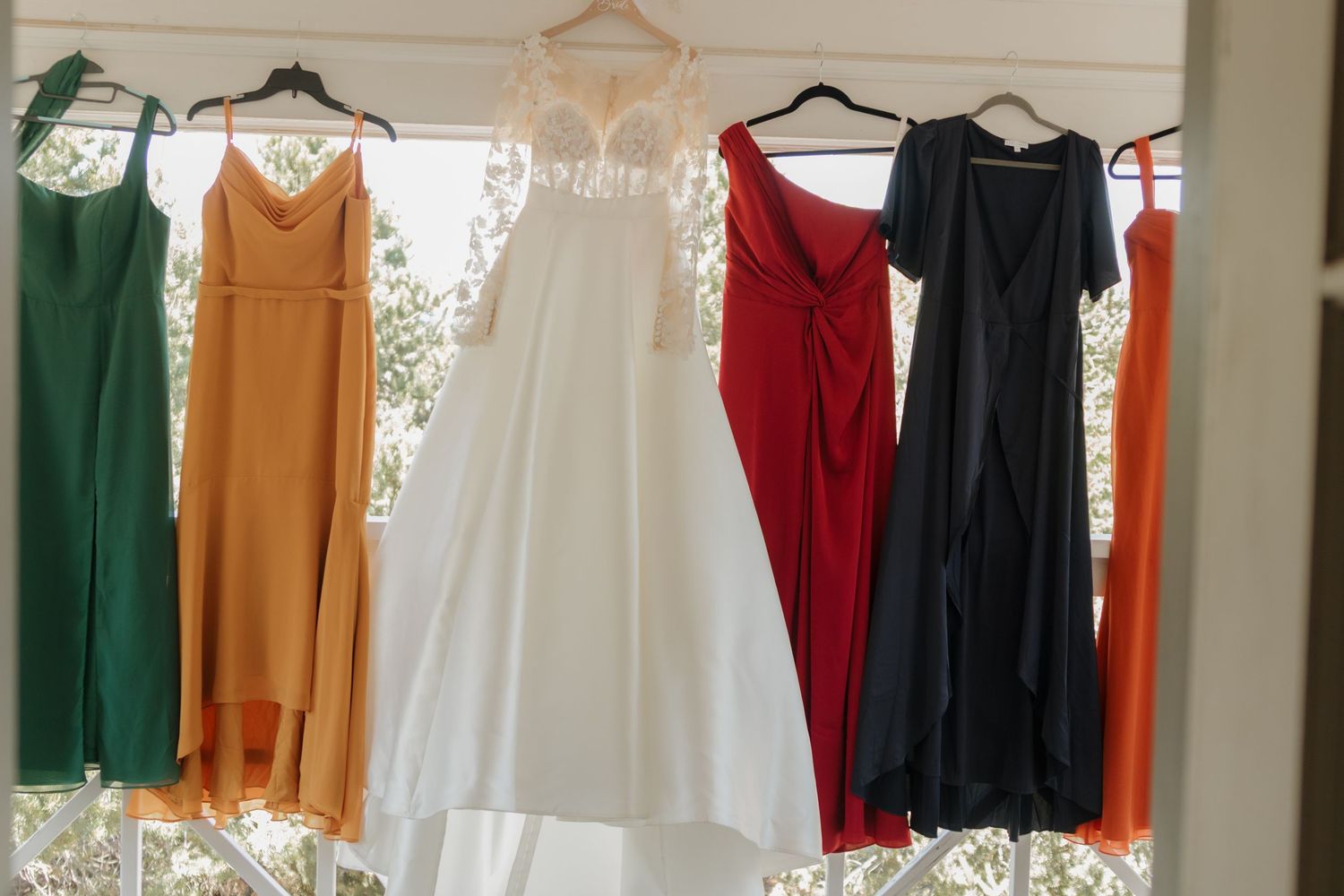 Colorful bridesmaid dresses hang in a row on hangers displaying various jewel tones.