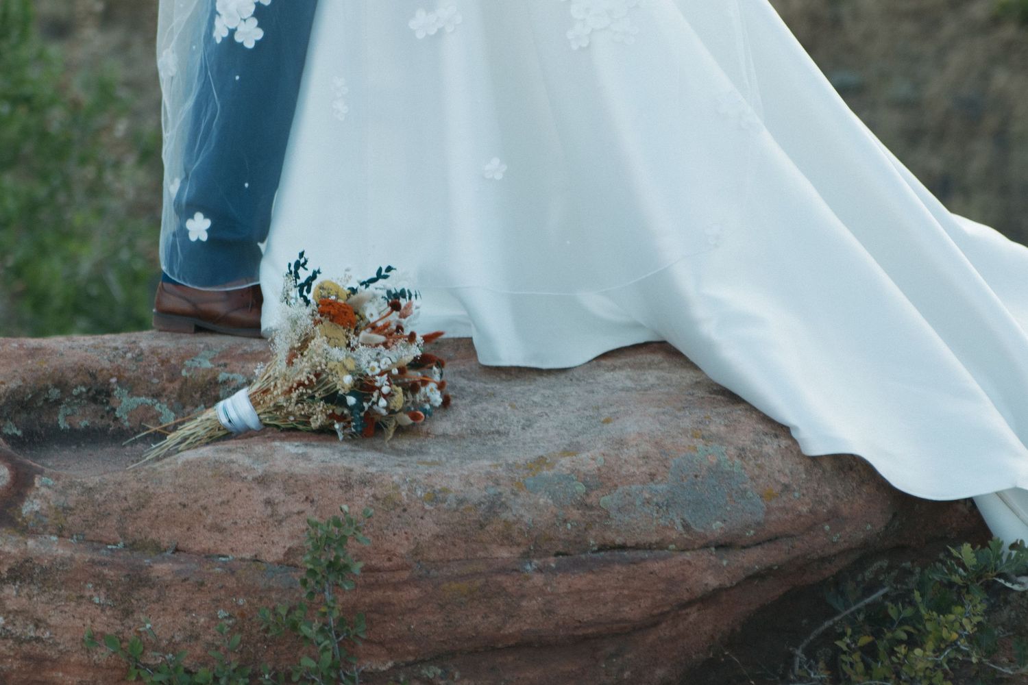 Wedding dress train elegantly draped over red desert rocks with floral accents.