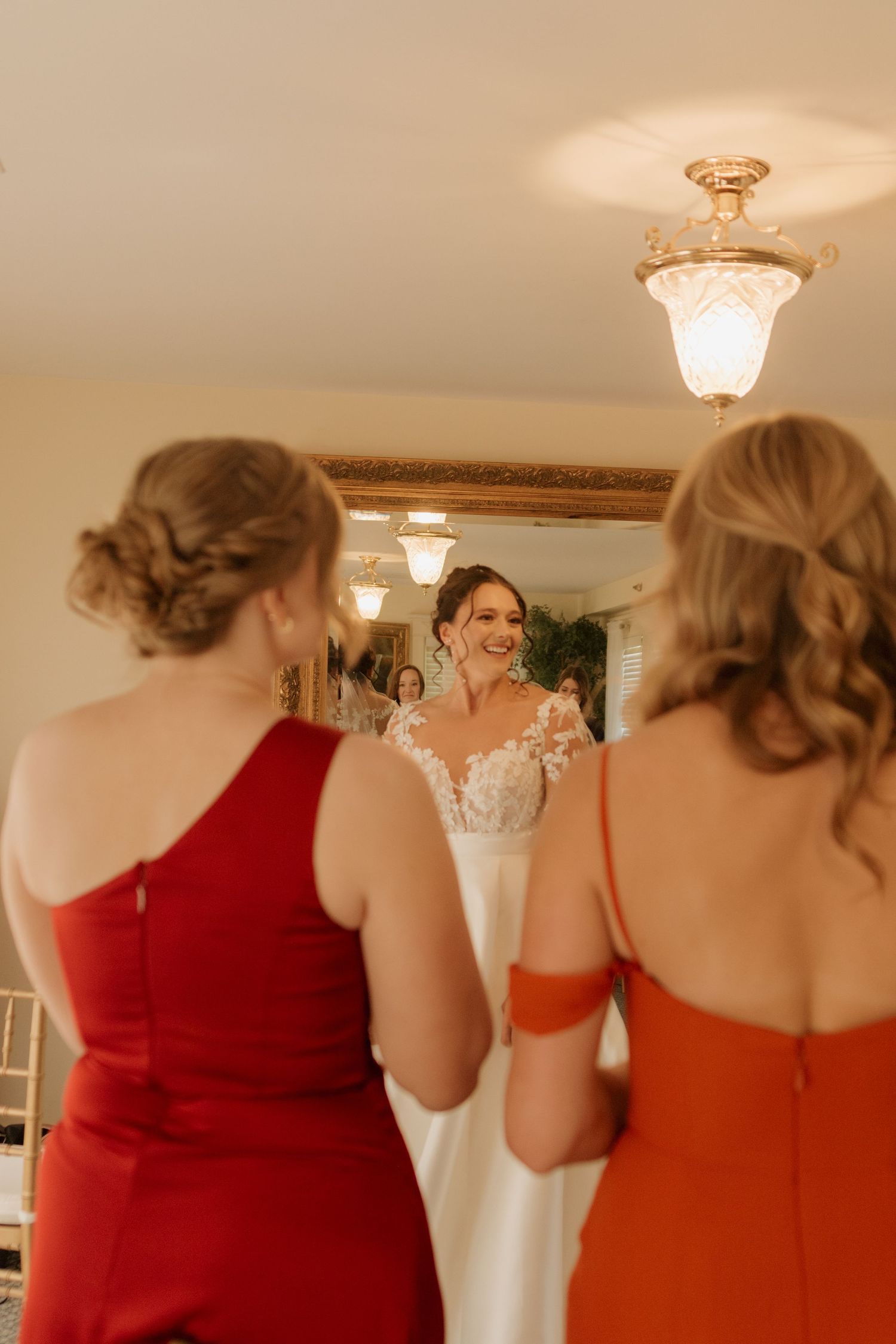 Bridesmaids in red dresses watching a bride try on her white wedding gown.