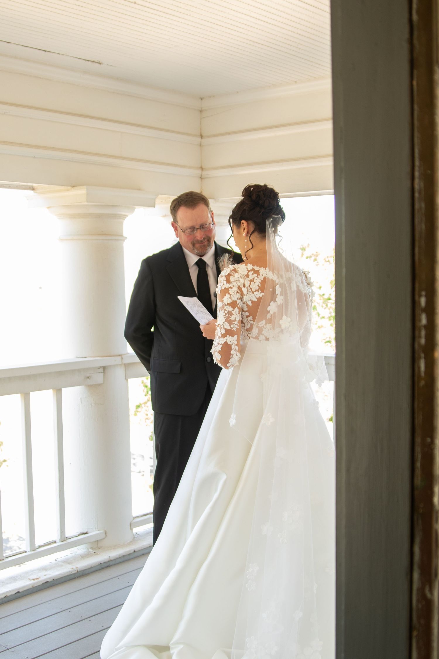 Emotional wedding first look between couple on covered porch with white railings.