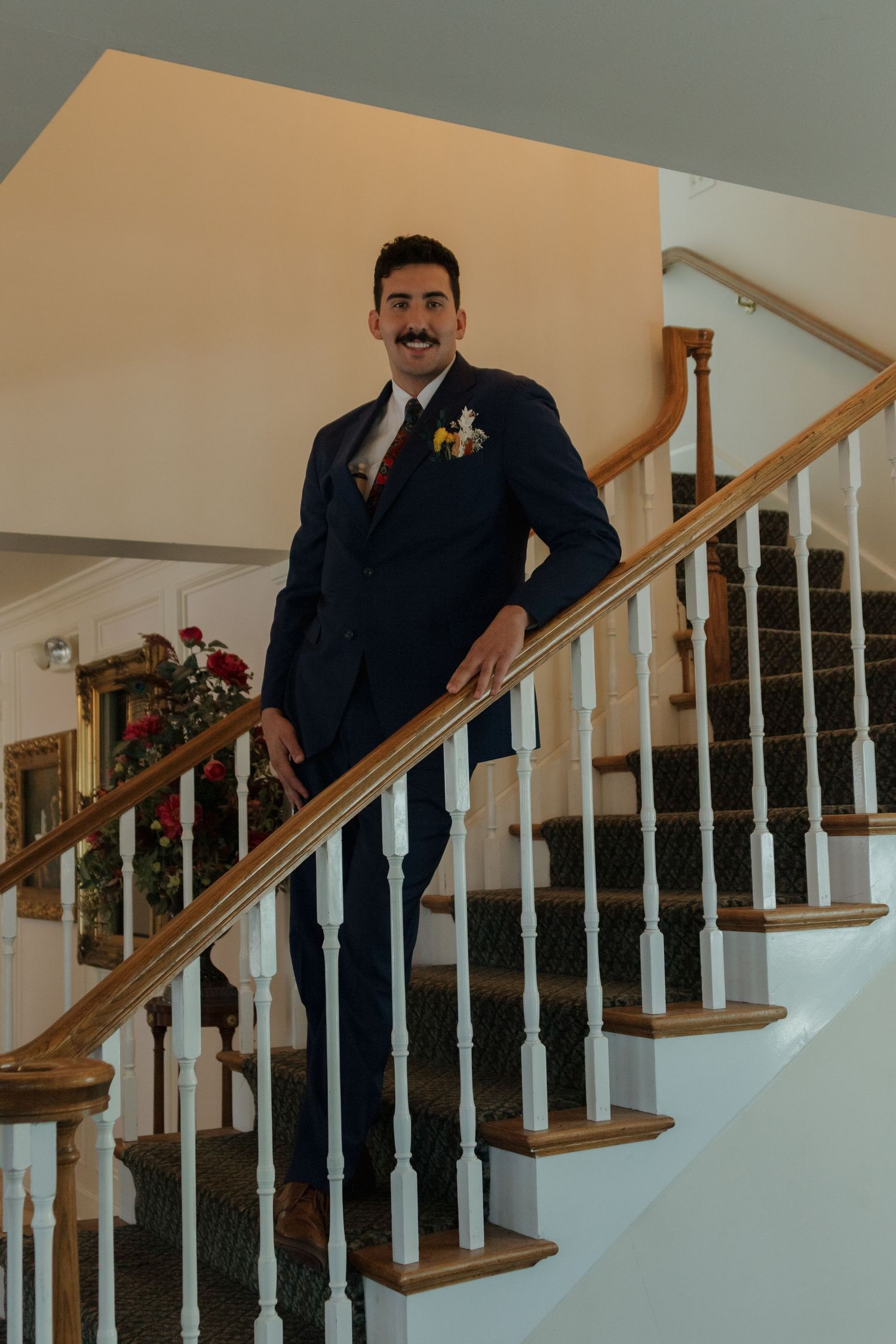 Groomsmen in formal attire stand along an elegant wooden staircase with white railings.