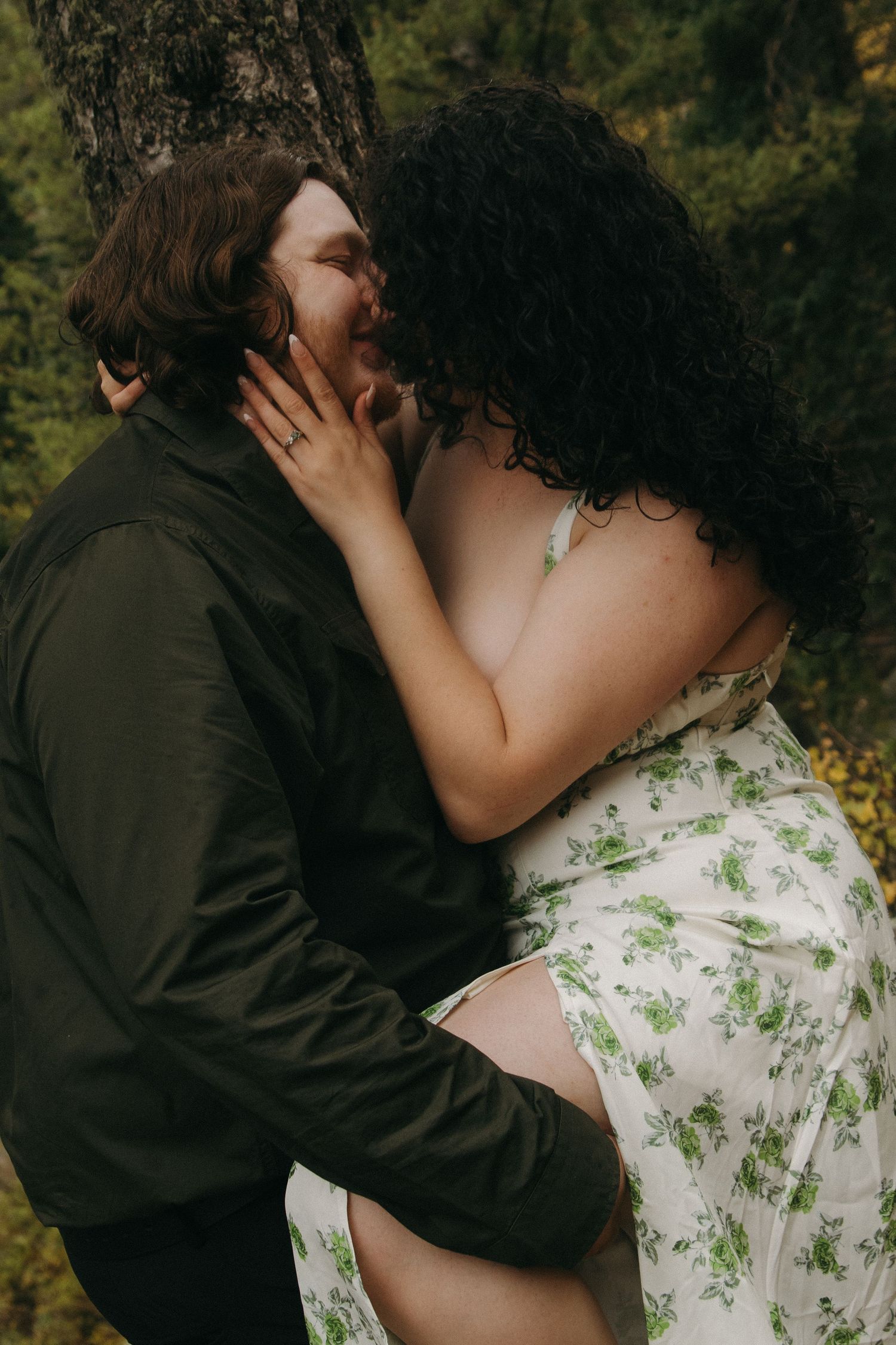 An intimate moment shared between a couple in a forest, with one wearing a floral dress.
