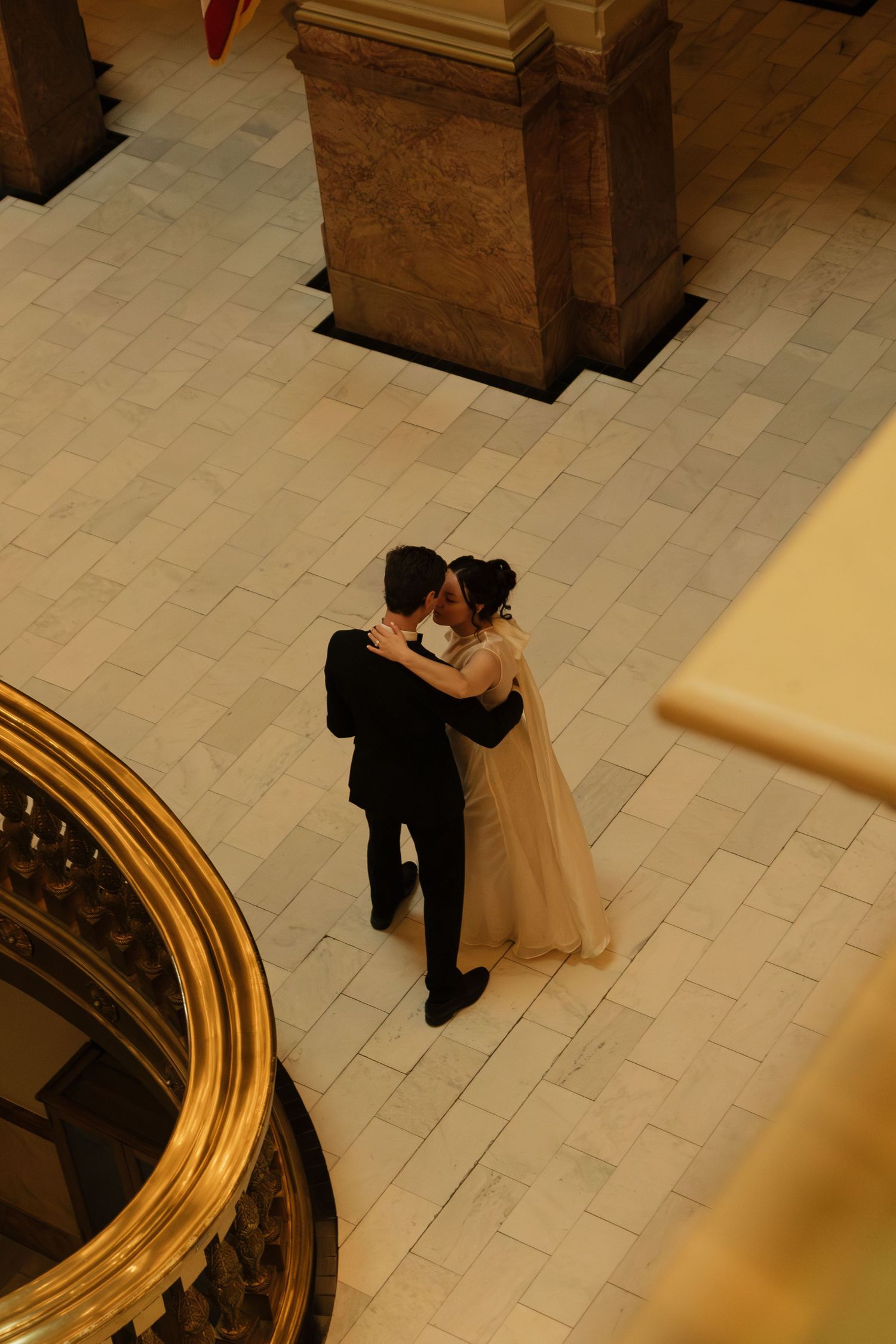 An overhead view of a couple dancing on a tiled floor beside a golden railing.