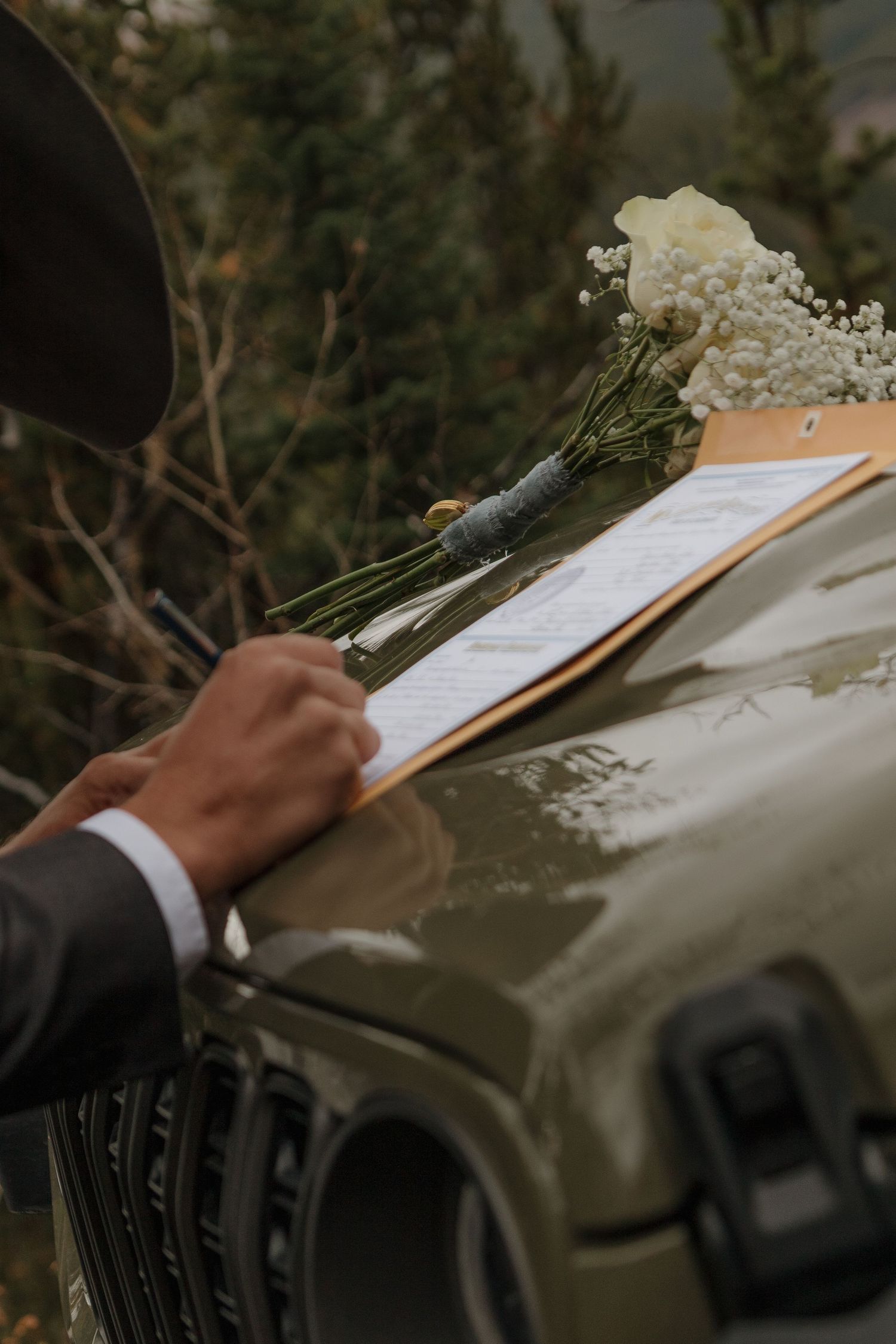 Close-up of hands signing wedding documents with a bouquet in the background.