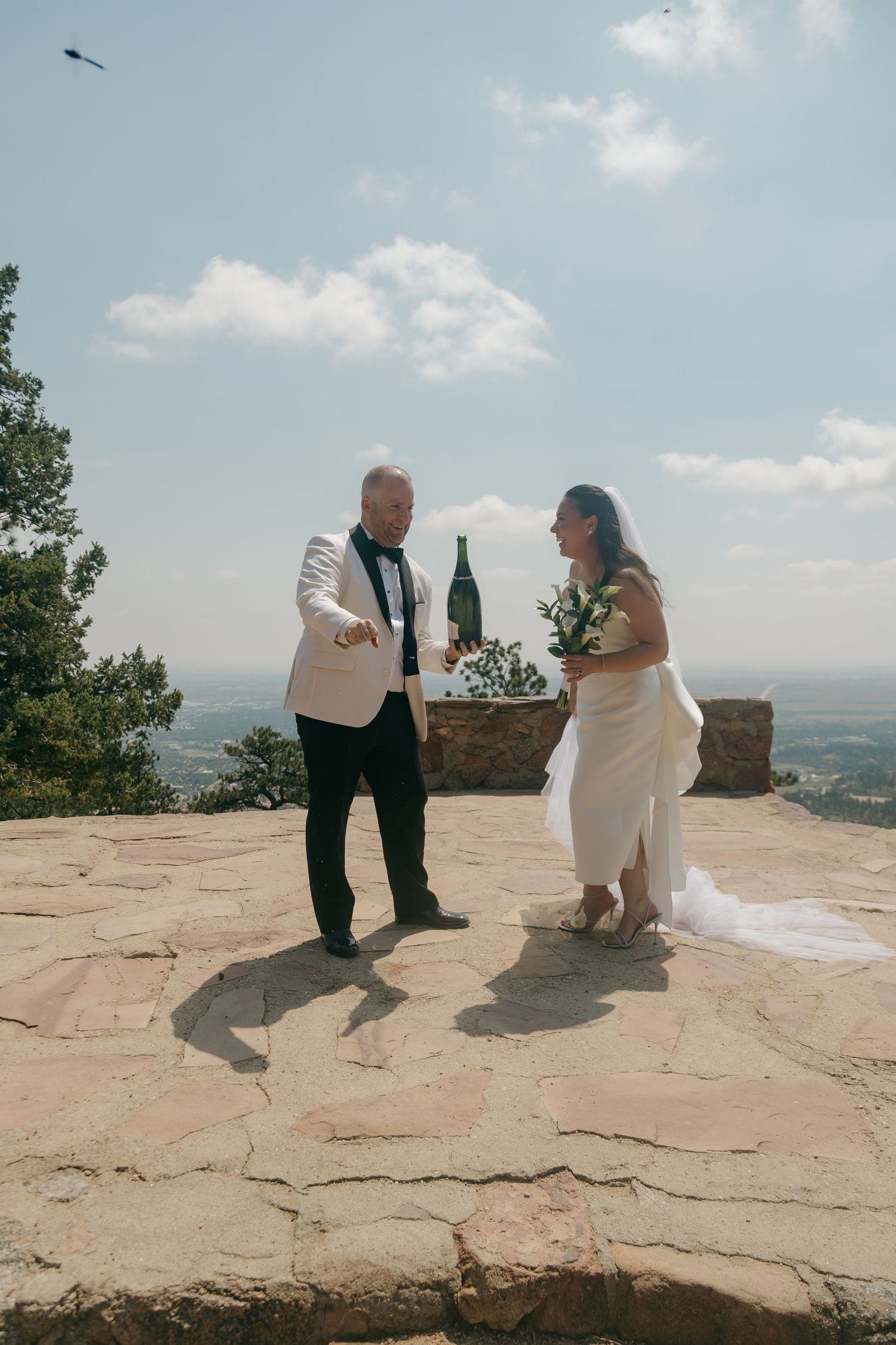 Newlyweds celebrating with champagne on a scenic mountain overlook after their outdoor wedding ceremony.