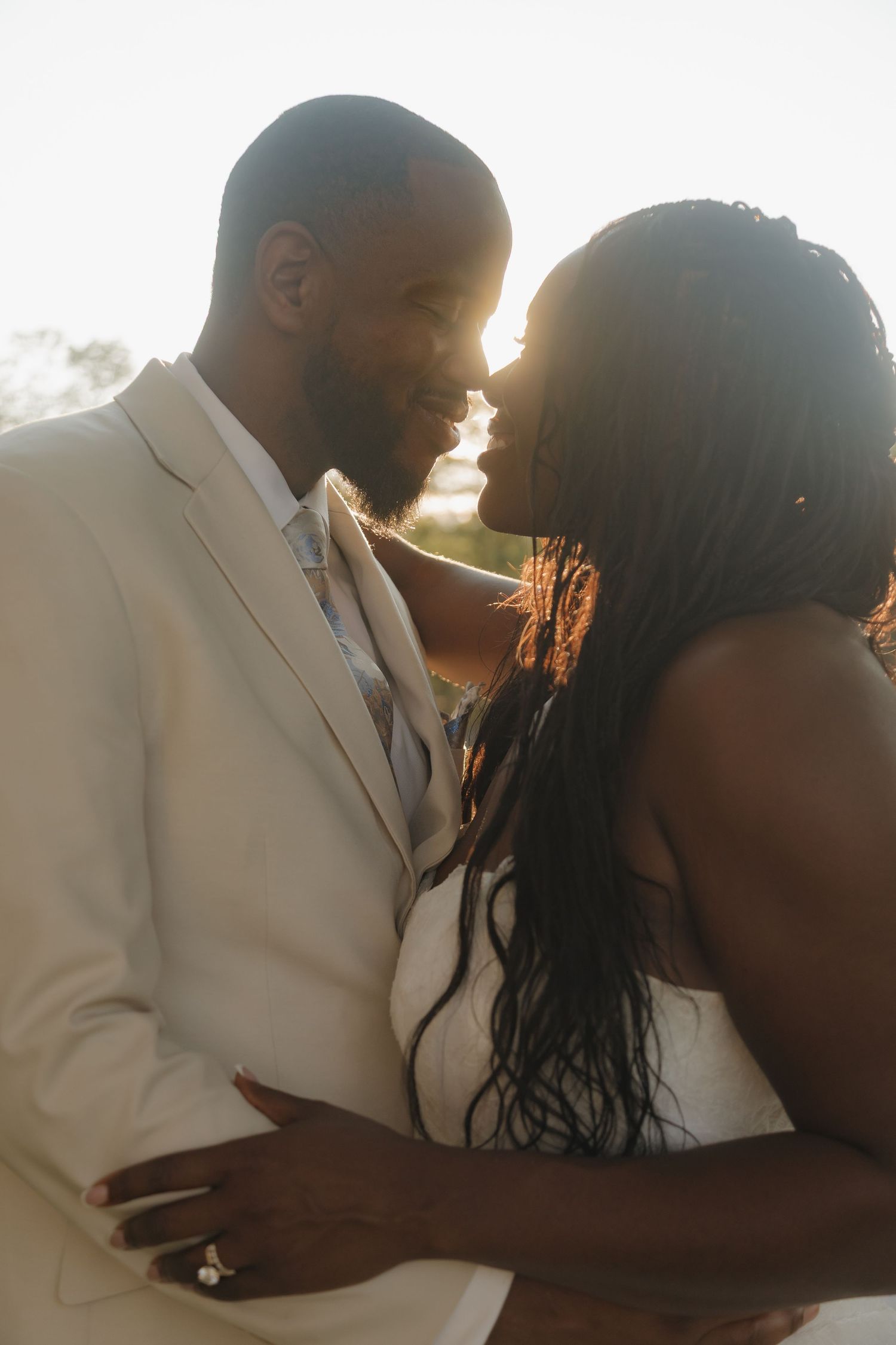 Black bride and groom share a romantic nose-to-nose moment in warm glowing backlit sunlight on their wedding day.