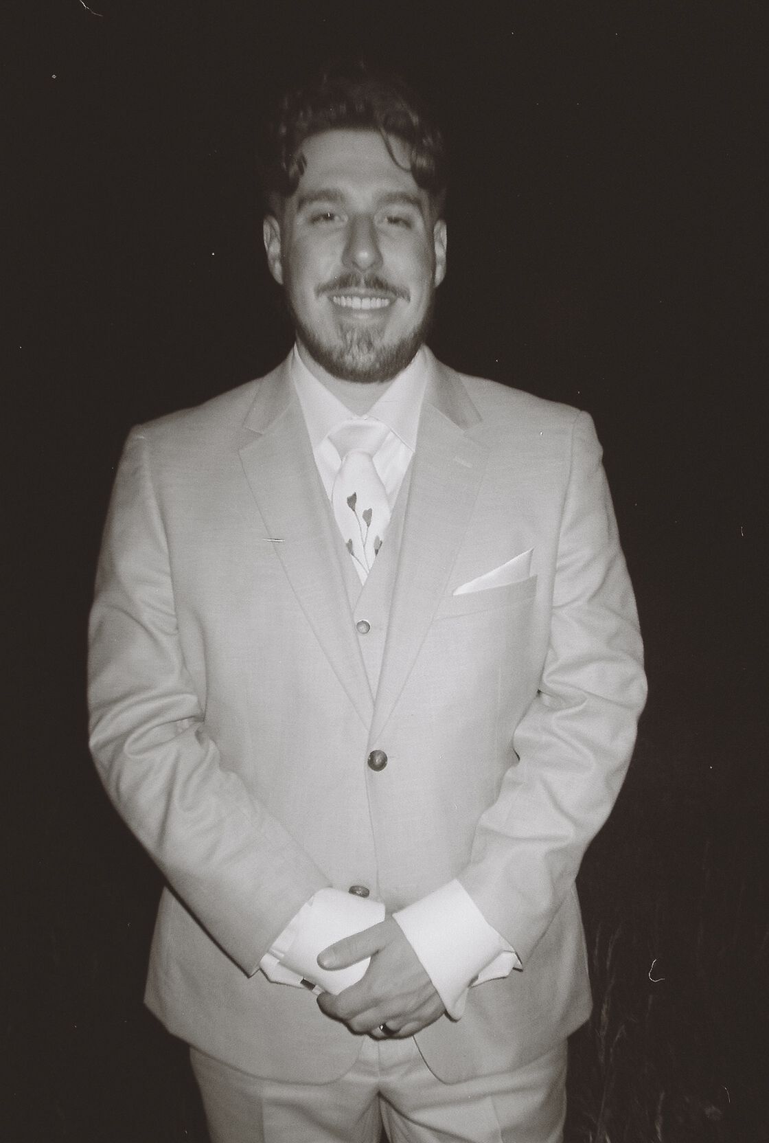 Black and white portrait of smiling groom in light gray three-piece suit with tie and pocket square.