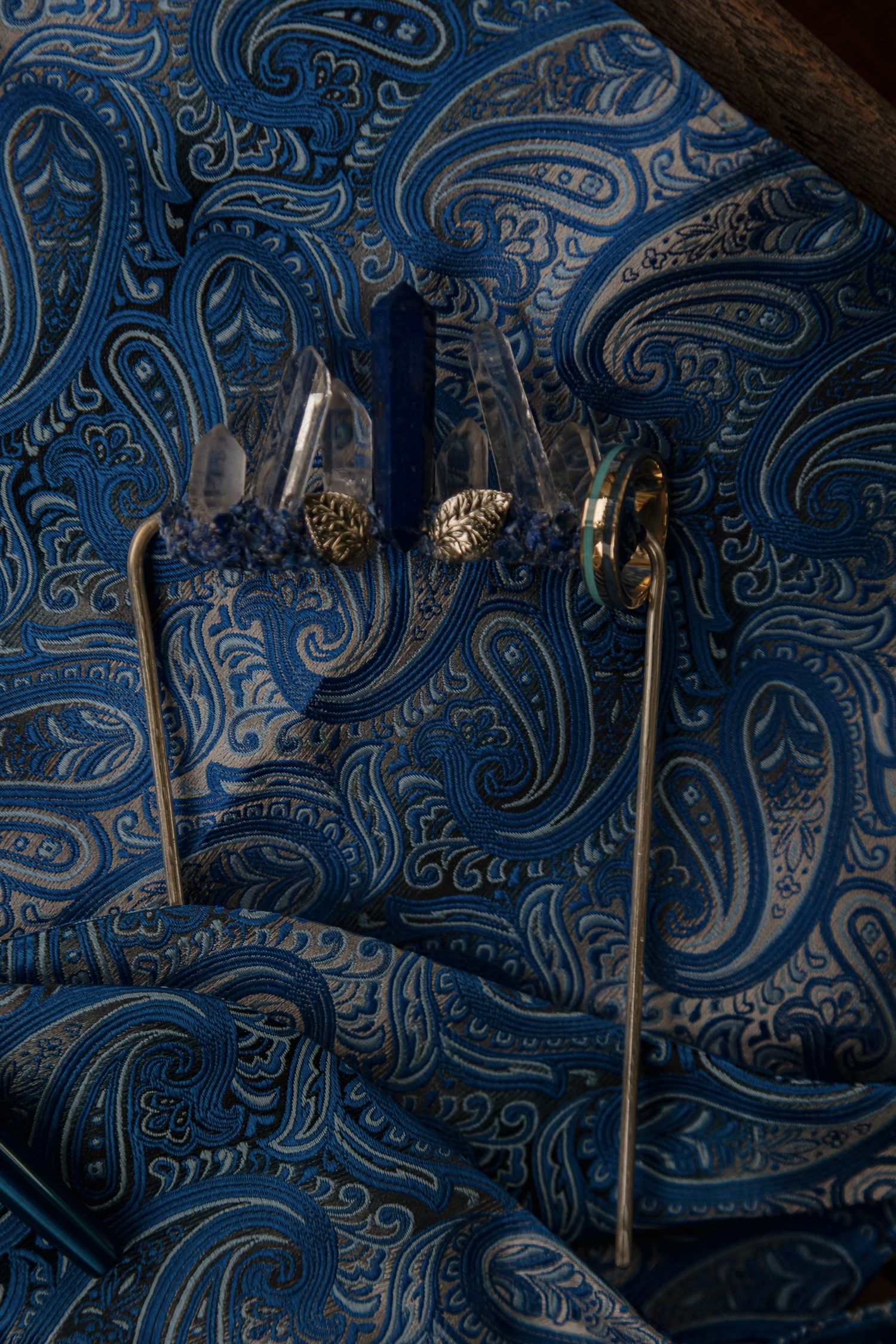 Close-up of a blue paisley pocket square with crystal and gold accessories on a wedding suit jacket.