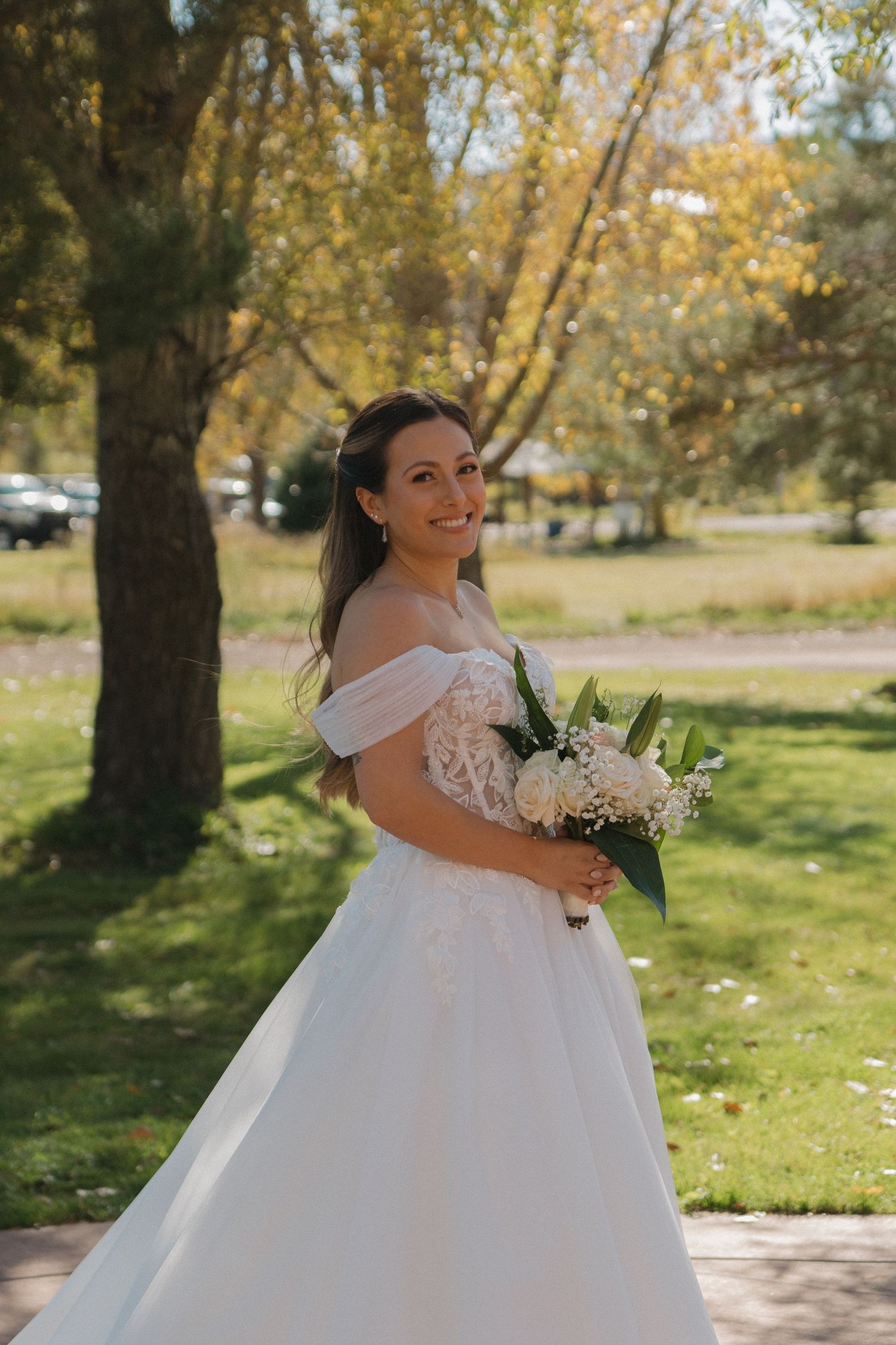 A bride in a white ball gown poses outdoors among autumn trees with golden leaves.