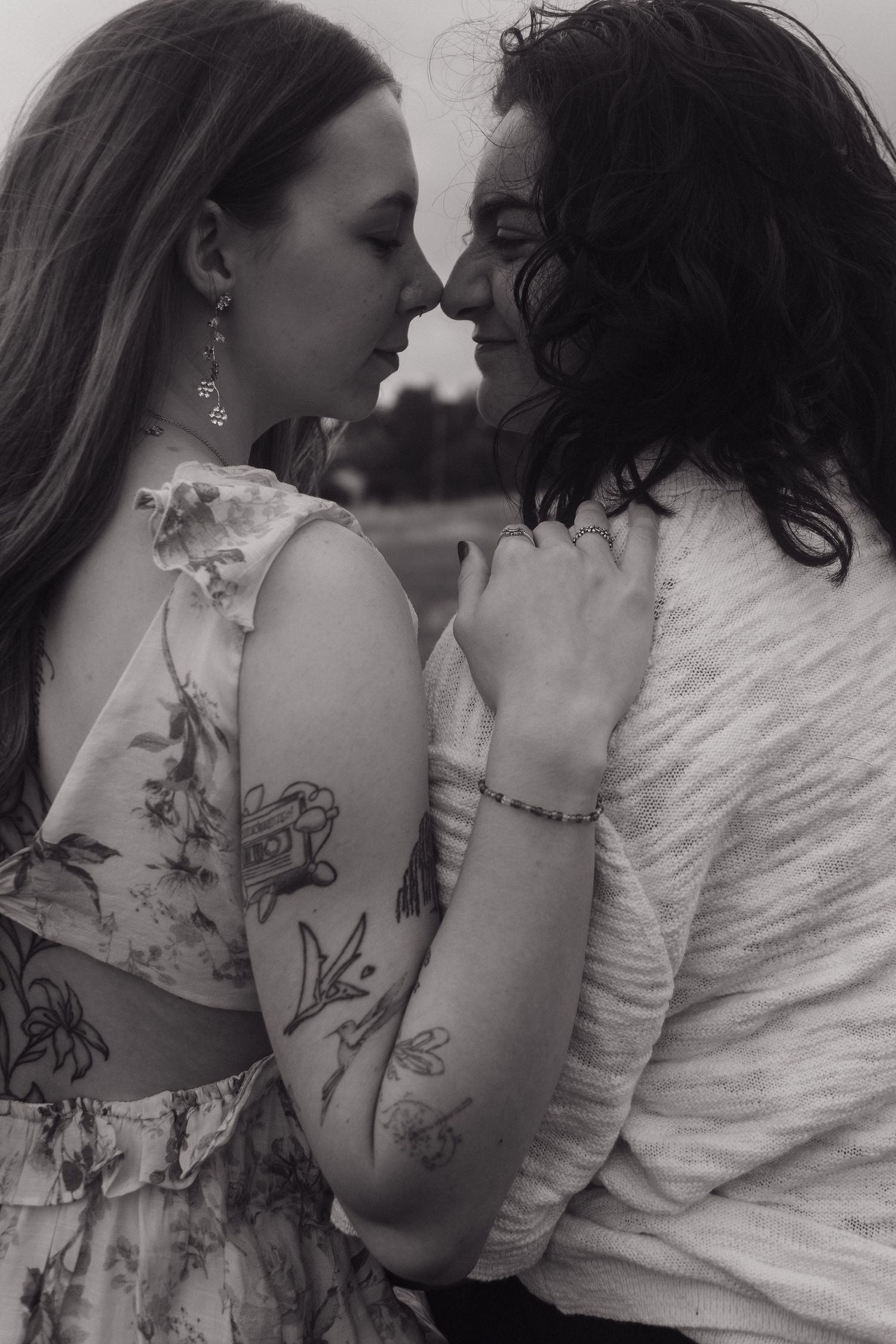 Black and white close-up of two women with tattoos leaning in for a kiss outdoors.