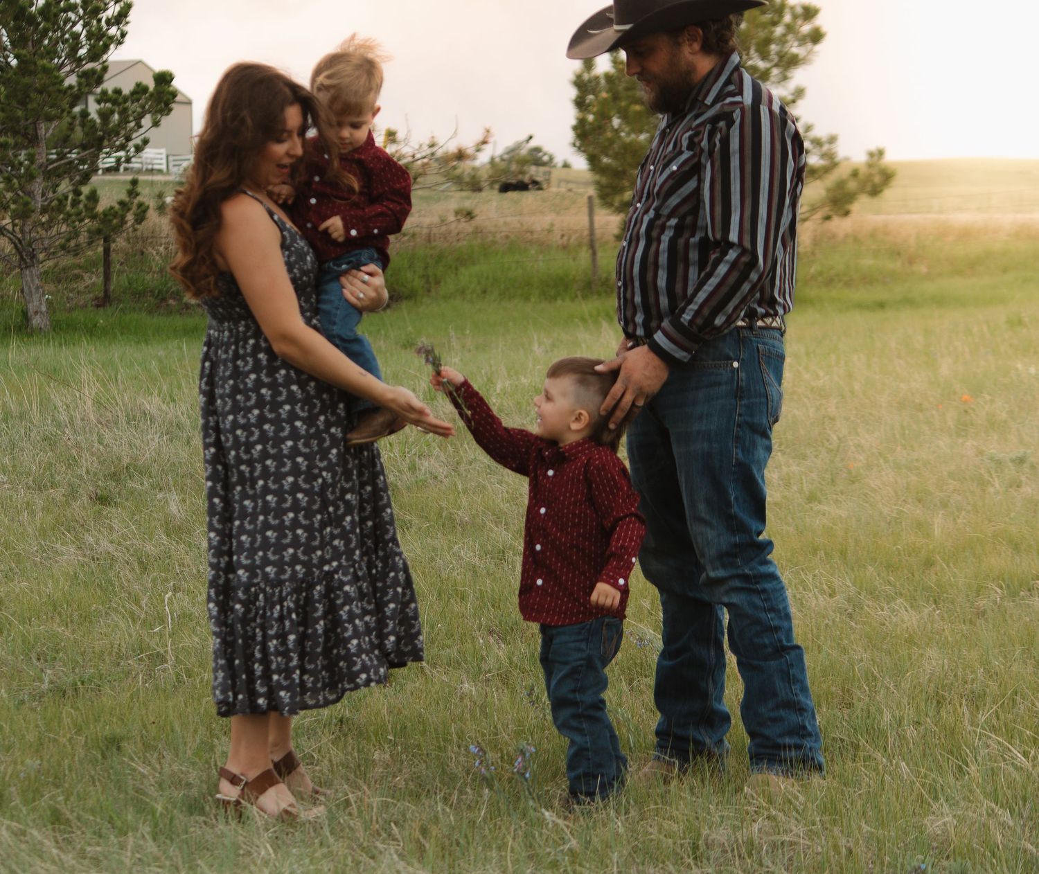 Casual outdoor family scene with western attire in a grassy field at golden hour.