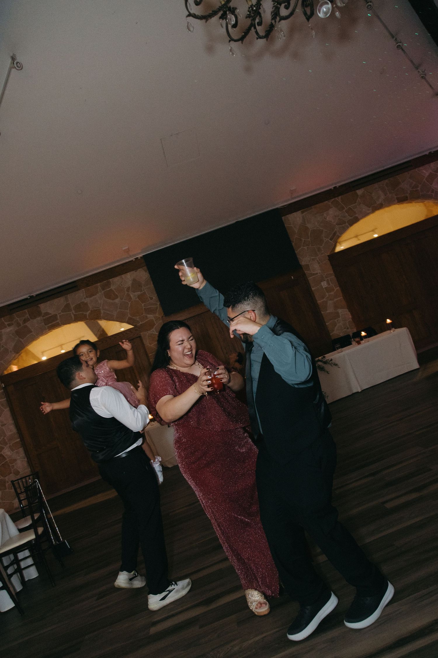 Joyful wedding guests dancing energetically on the dance floor at a rustic indoor reception.