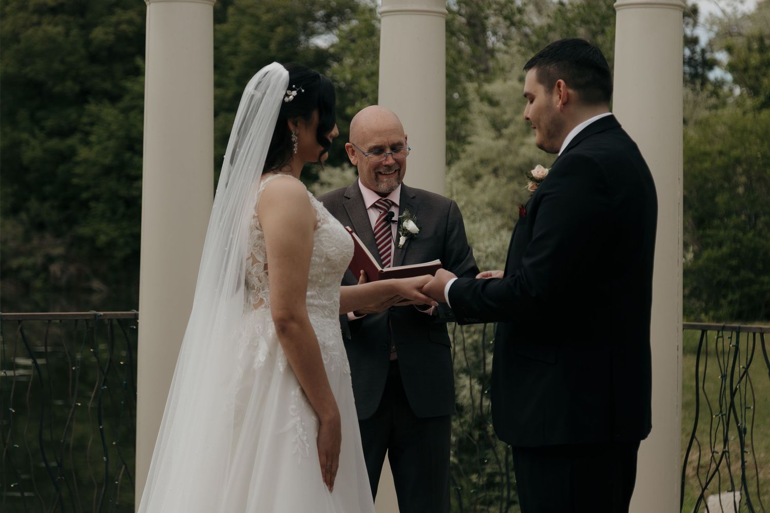 Bride and groom hold hands during intimate outdoor wedding ceremony with officiant.