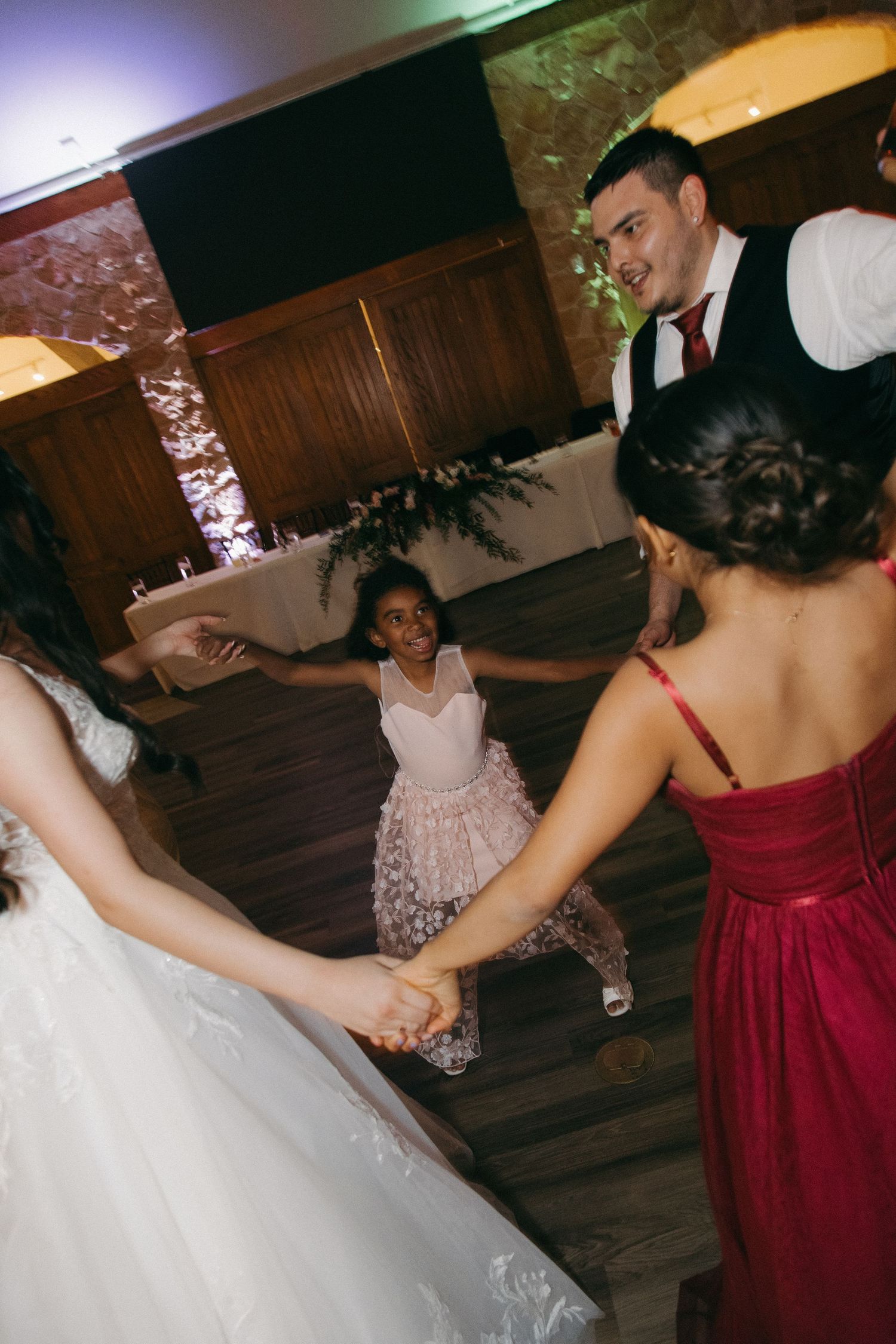 Bride, groom, flower girl, and bridesmaid hold hands in a circle on the wedding dance floor.