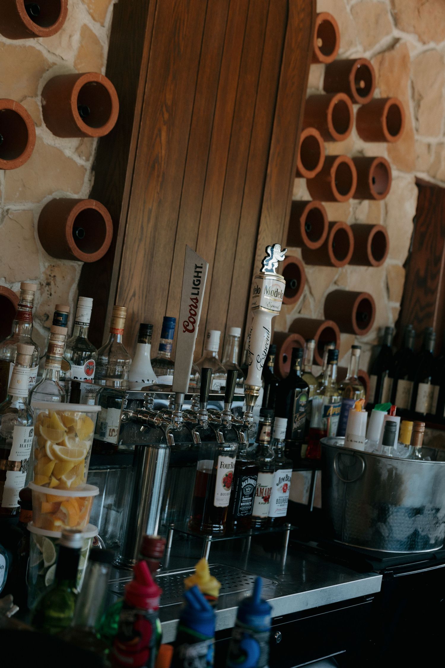 Wedding venue bar with Coors Light tap, liquor bottles, and decorative clay pipe wall display.
