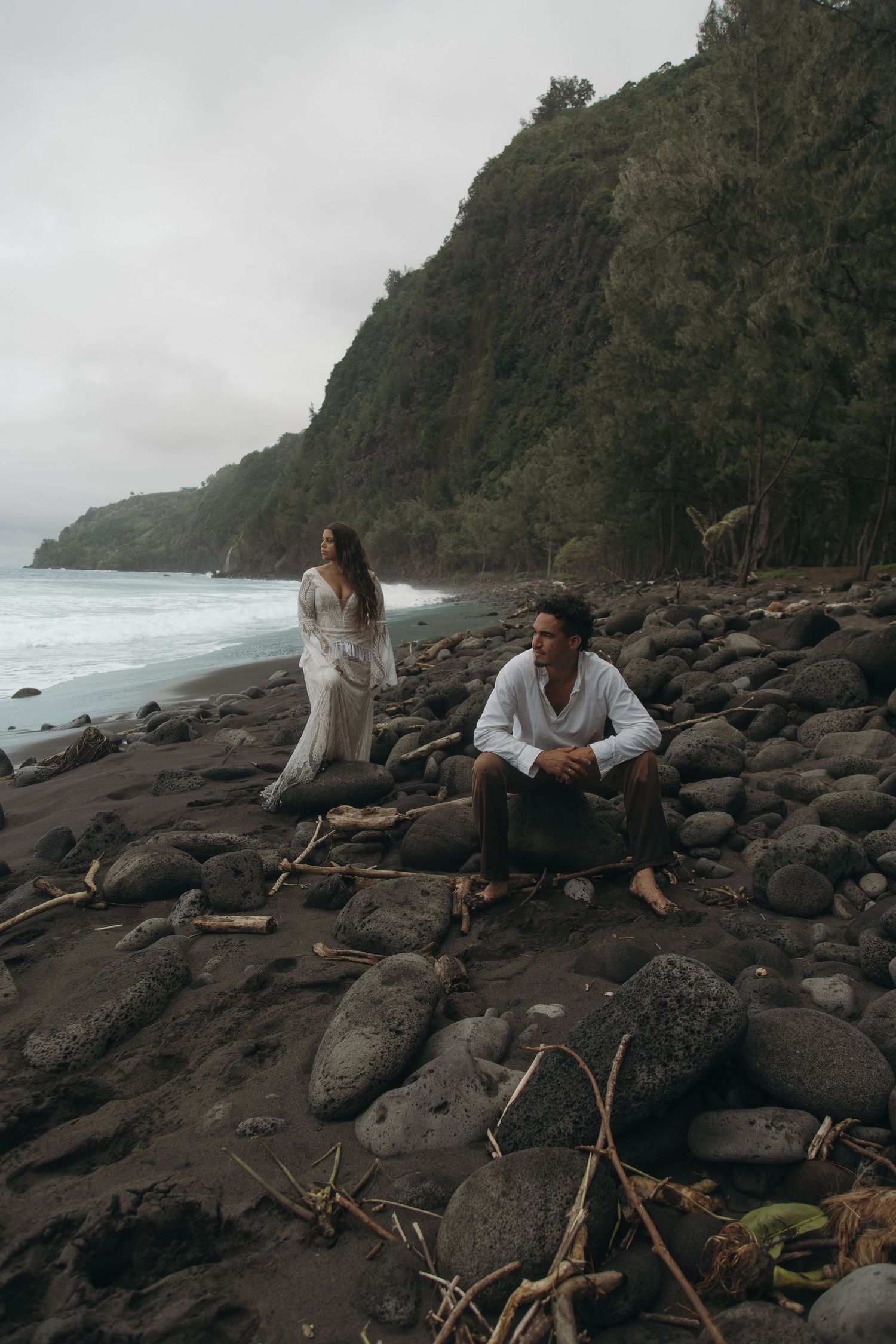 People relaxing on rocky volcanic beach with dramatic cliffs and ocean waves in Hawaii.