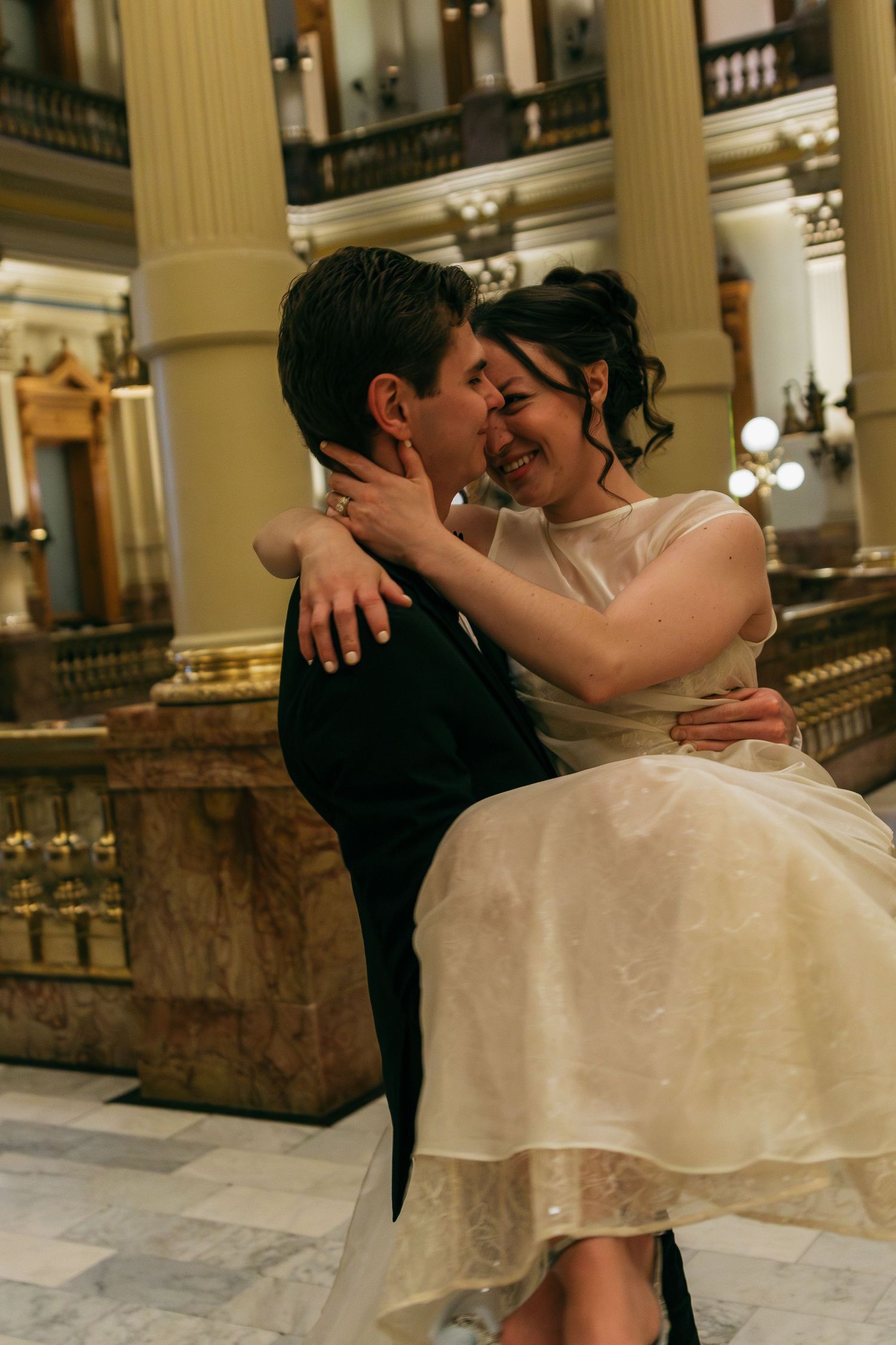 Romantic wedding couple embracing on marble floor in elegant historic building interior.
