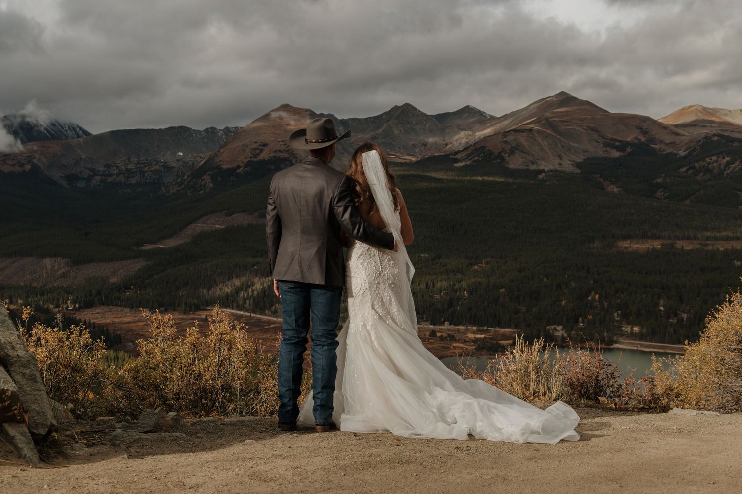 A couple stands together overlooking a mountain landscape during their wedding day.