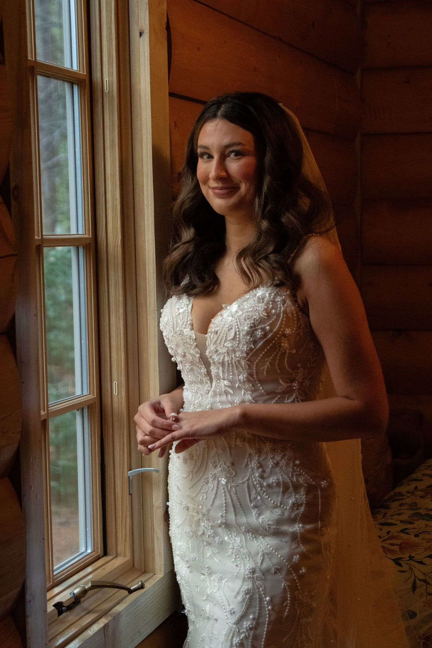 A stunning white lace wedding dress with intricate details photographed near a window in warm lighting.