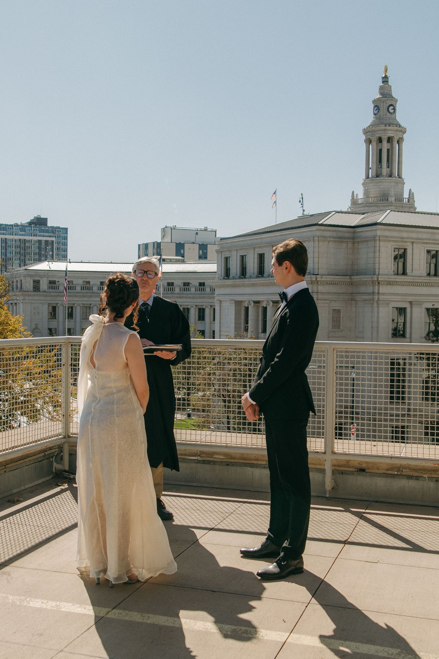 Wedding couple on a rooftop terrace with classical architecture and city skyline in background.