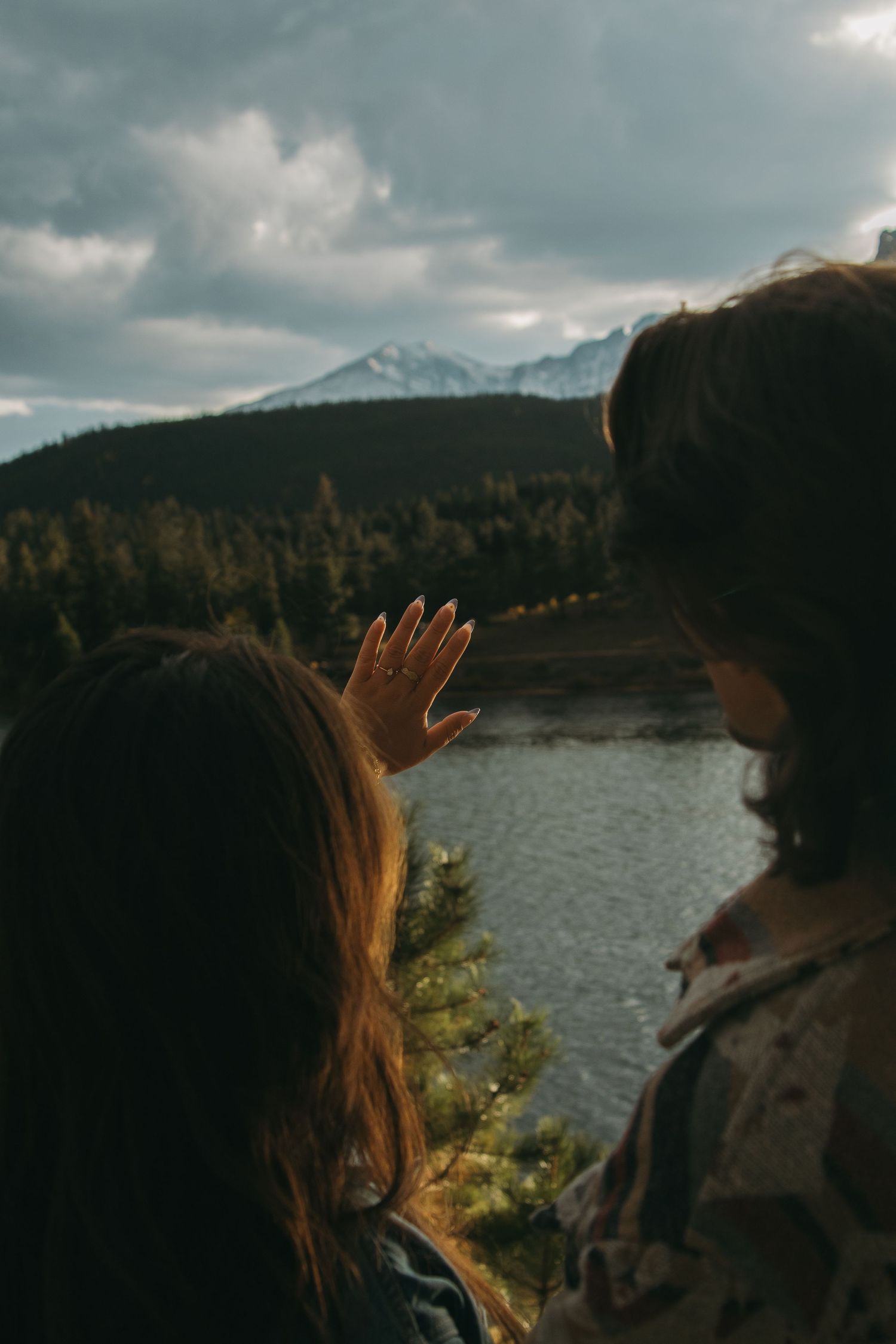 People admiring scenic mountain landscape with lake and forest under dramatic cloudy sky.