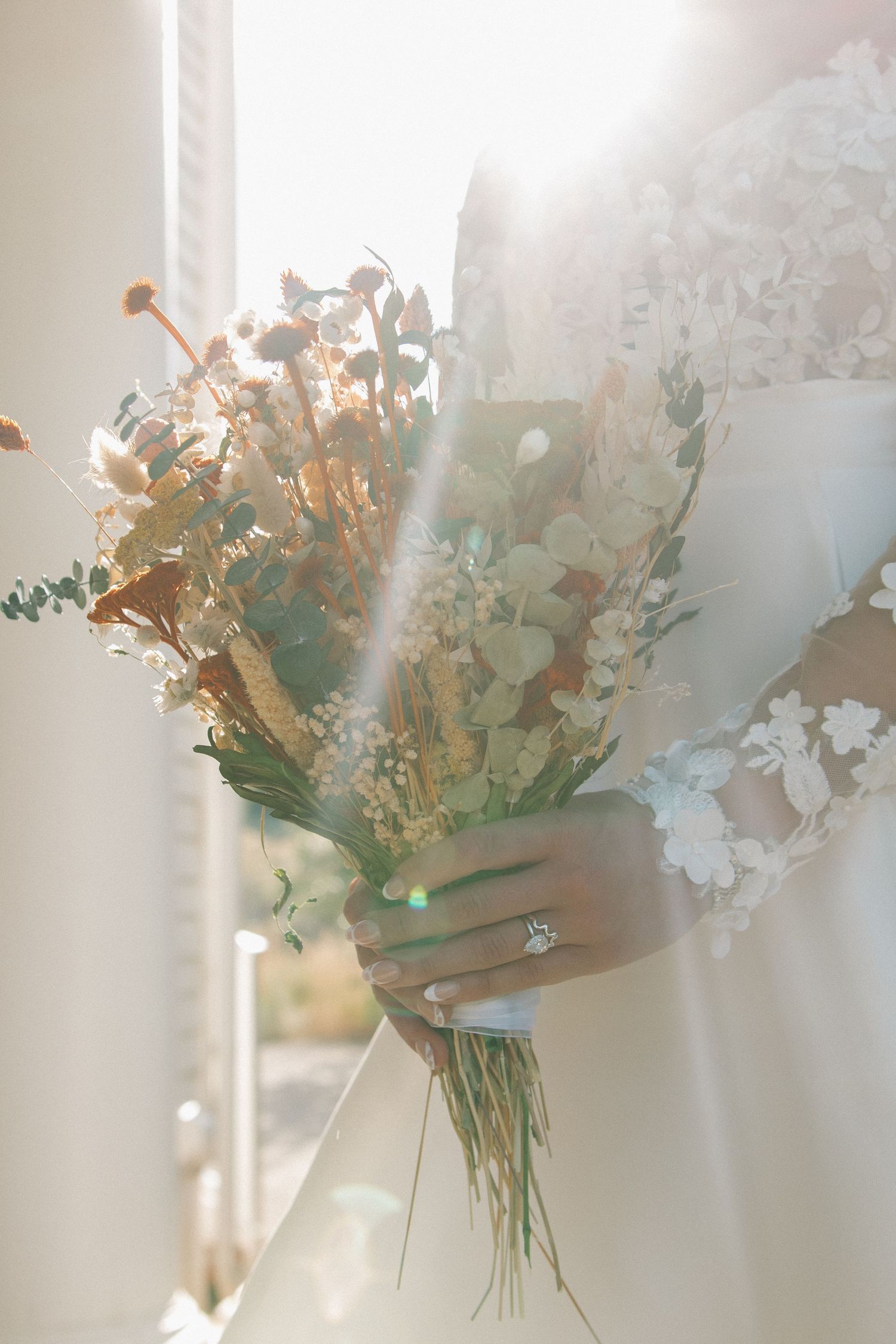A soft, ethereal floral arrangement of white blossoms and eucalyptus leaves bathed in dreamy natural light.