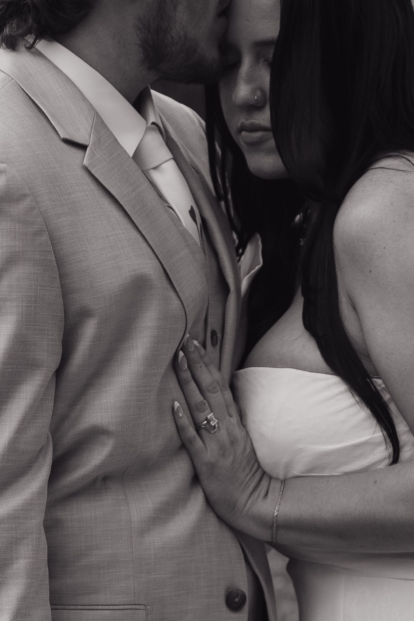 Black and white close-up of bride leaning into groom, showcasing her diamond engagement ring.