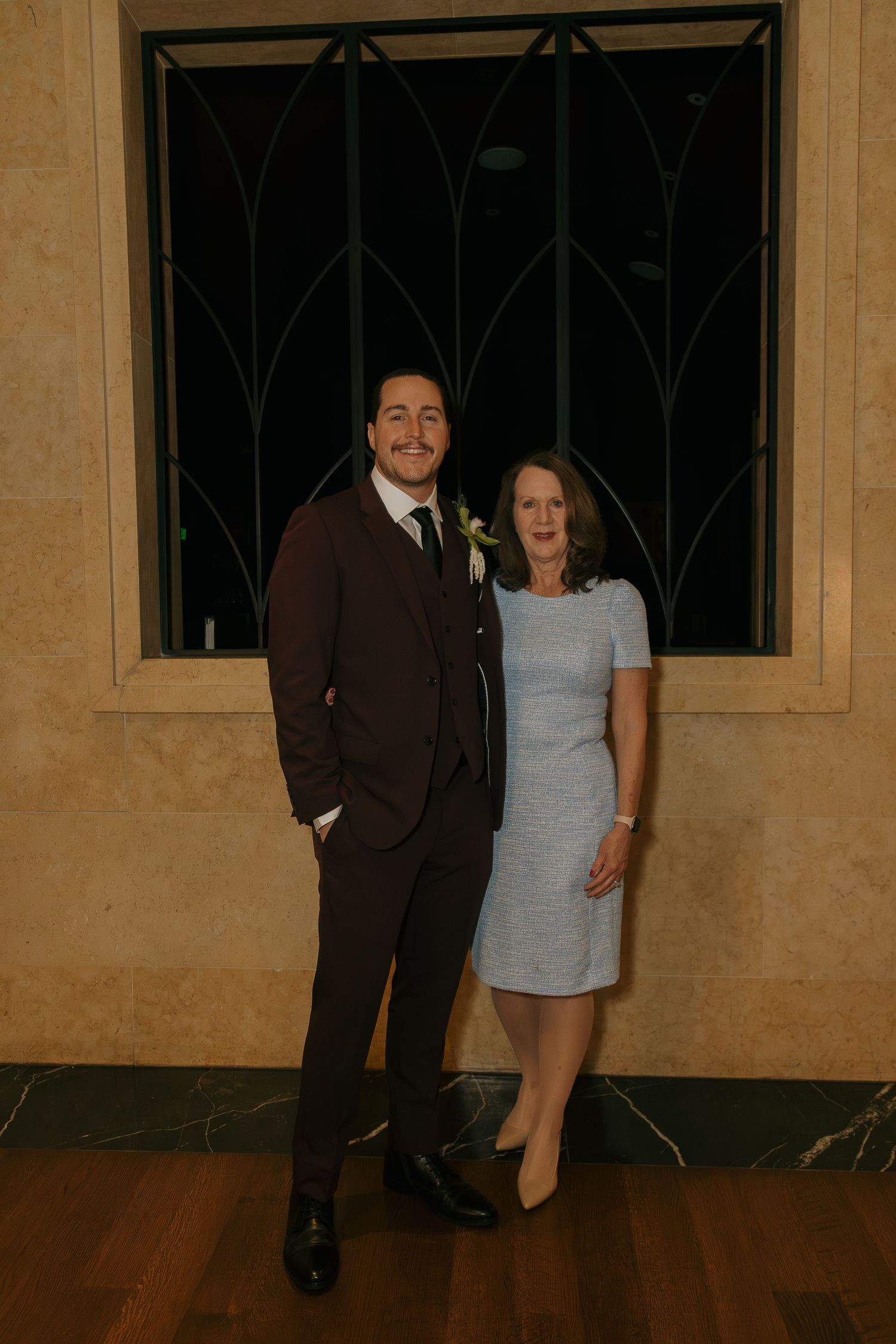 A man in a brown suit and woman in a blue dress posing together at a formal event.