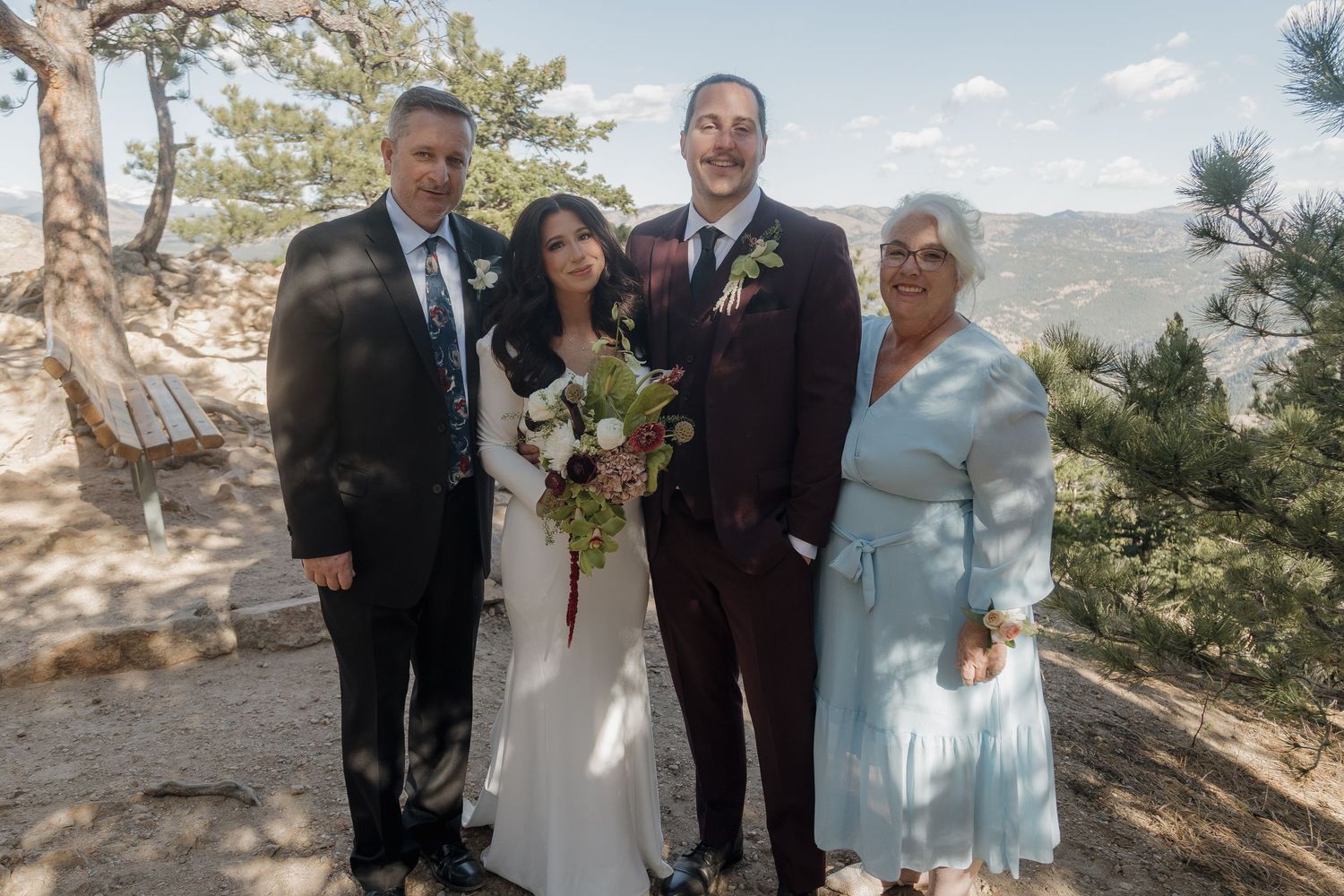 Wedding portrait of bride and groom with two family members against mountain backdrop outdoors.