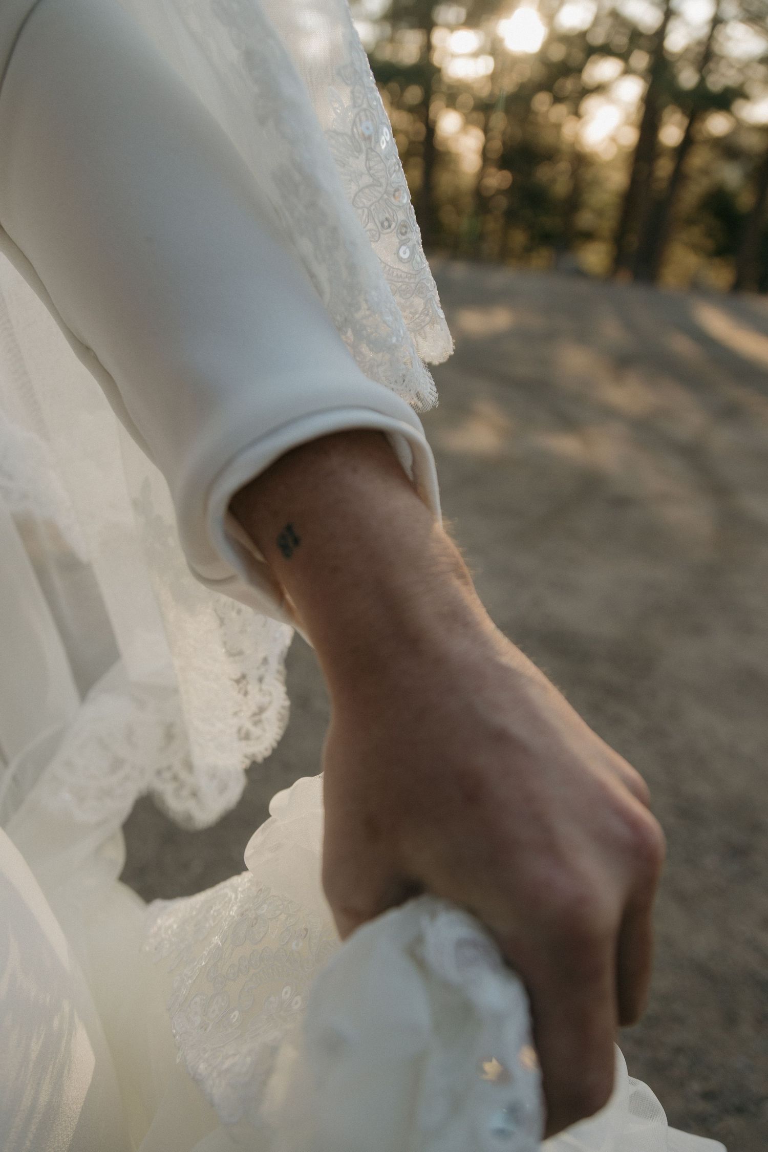 Close-up of a bride's lace wedding dress sleeve with a small tattoo on her wrist.
