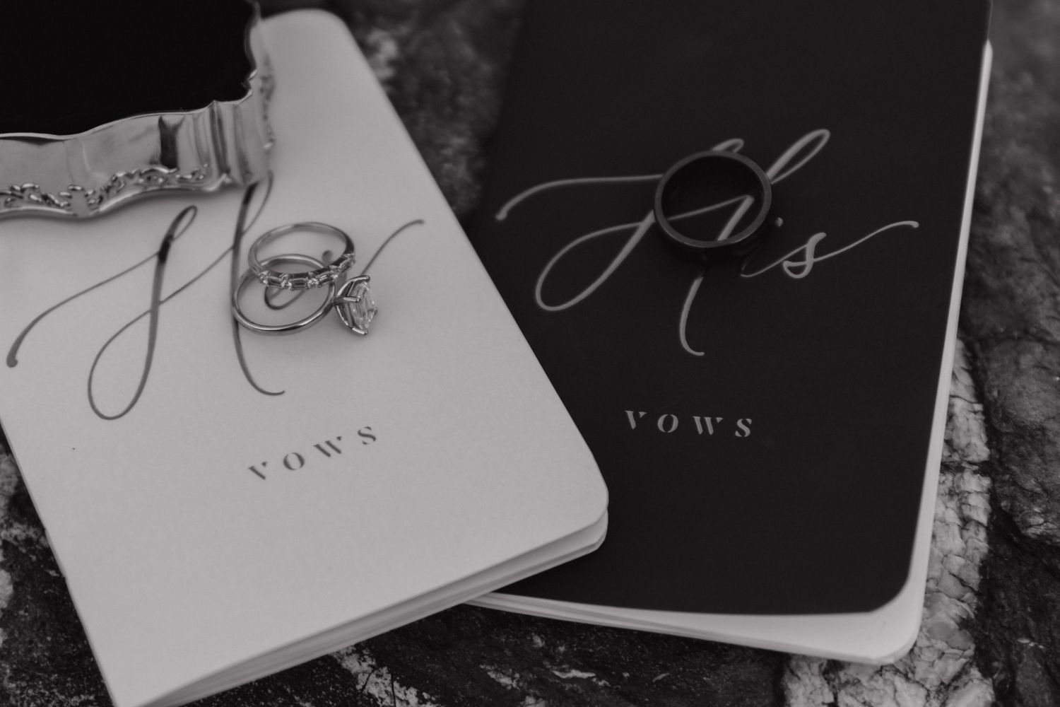 Black and white wedding vow books arranged artistically on a textured surface.