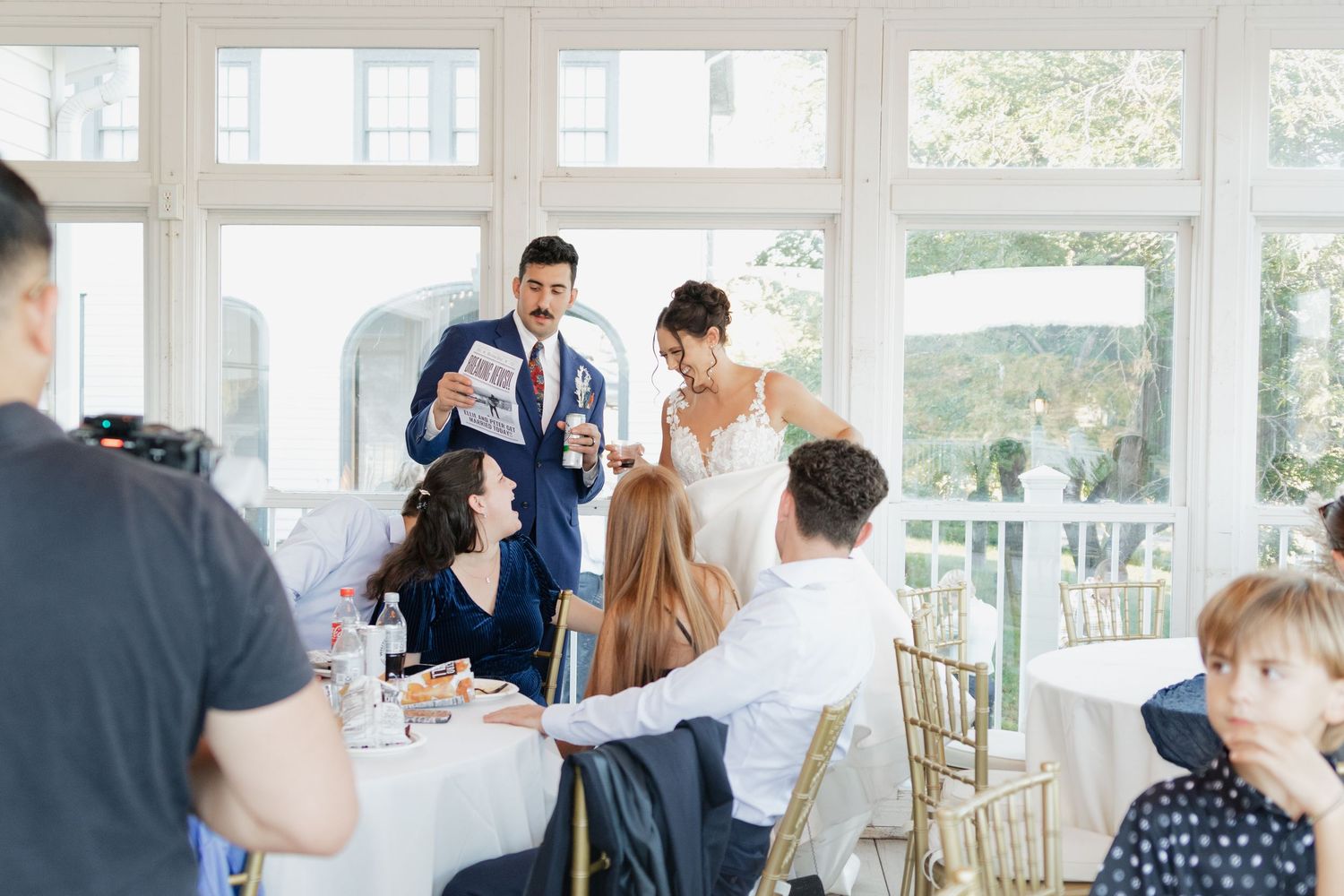 Wedding reception venue decorated with bright windows and elegant gold chairs.