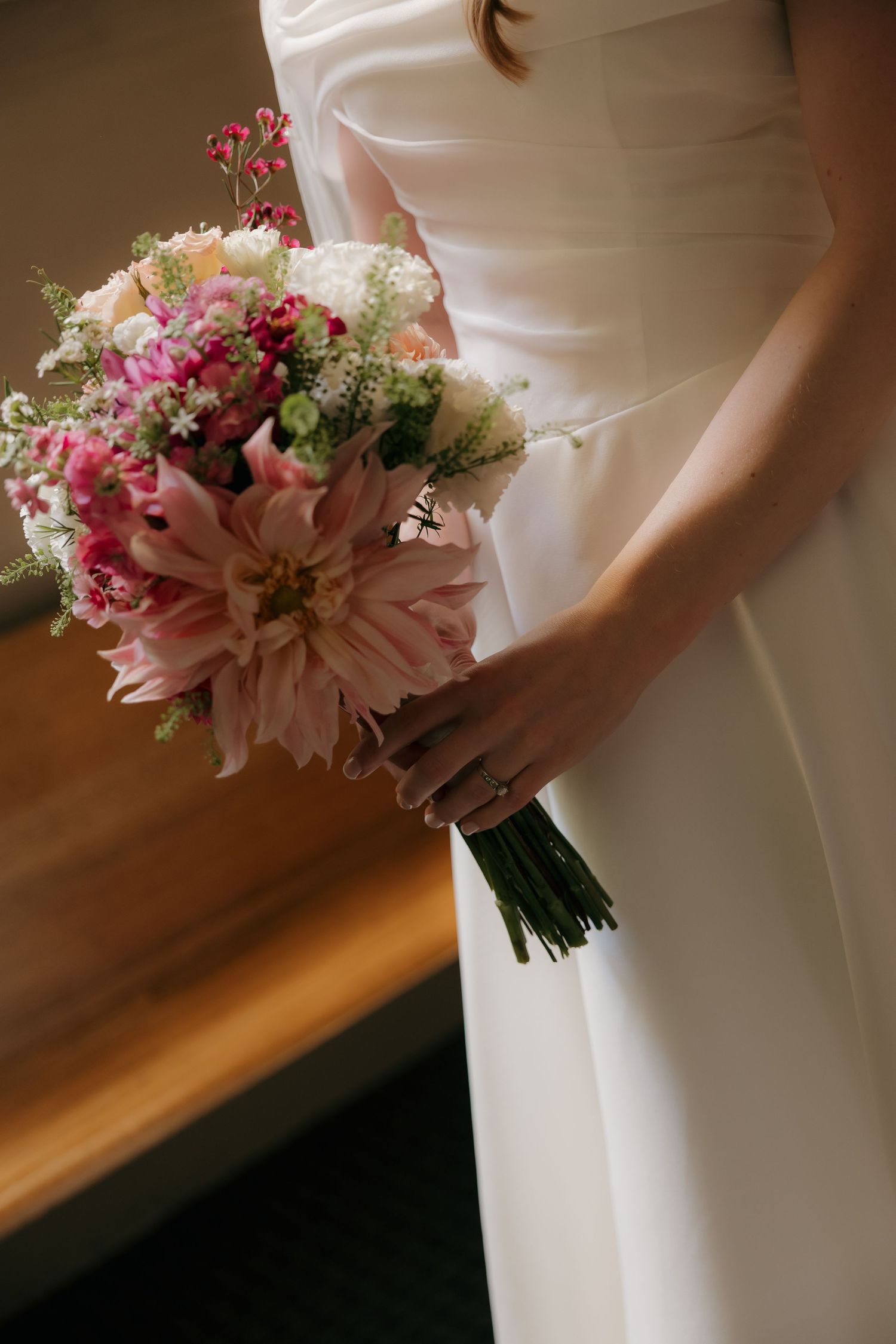 Bride in white gown holding a pink and blush wedding bouquet featuring dahlias and wildflowers.