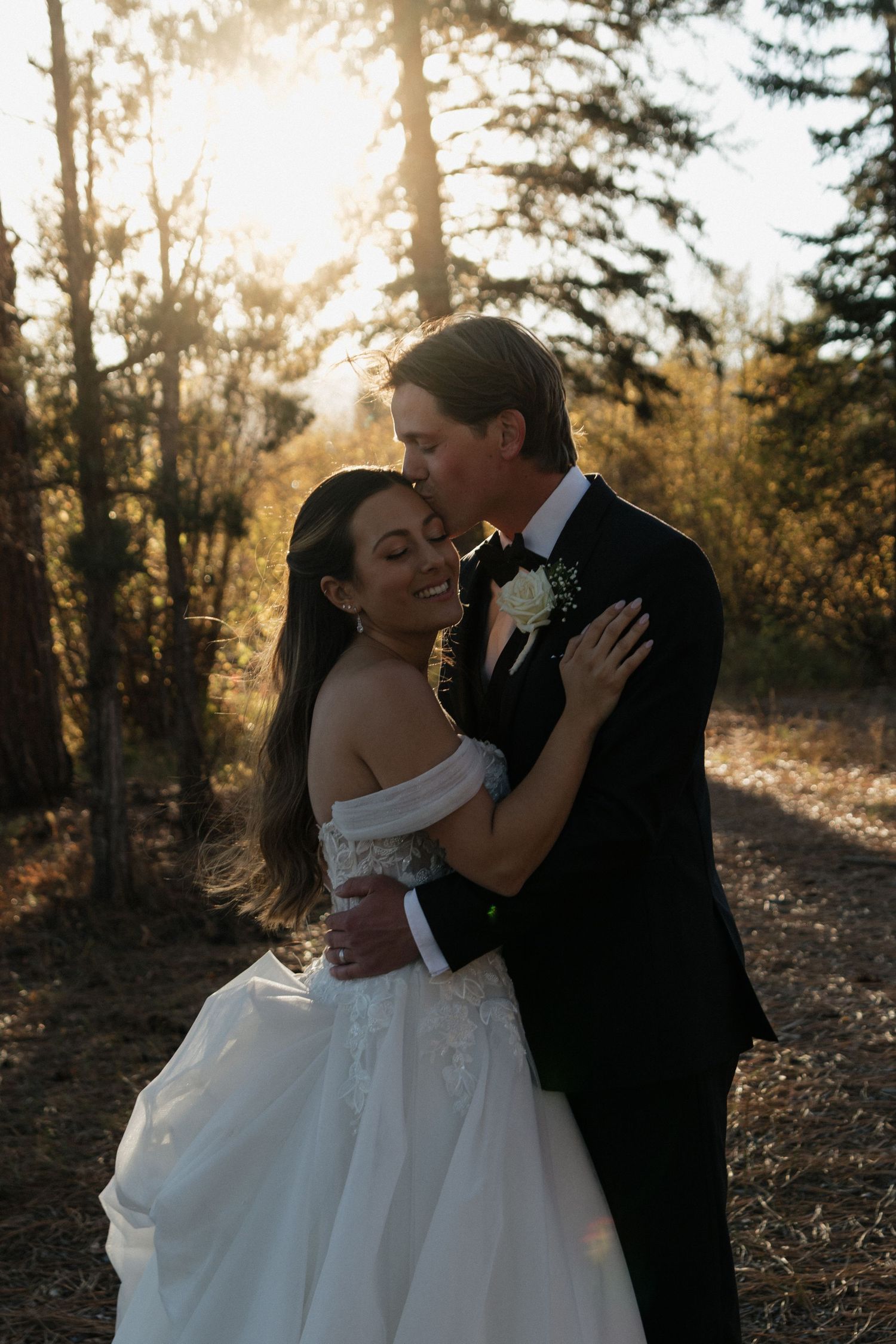 Romantic sunset wedding portrait in a wooded setting with golden light filtering through trees.