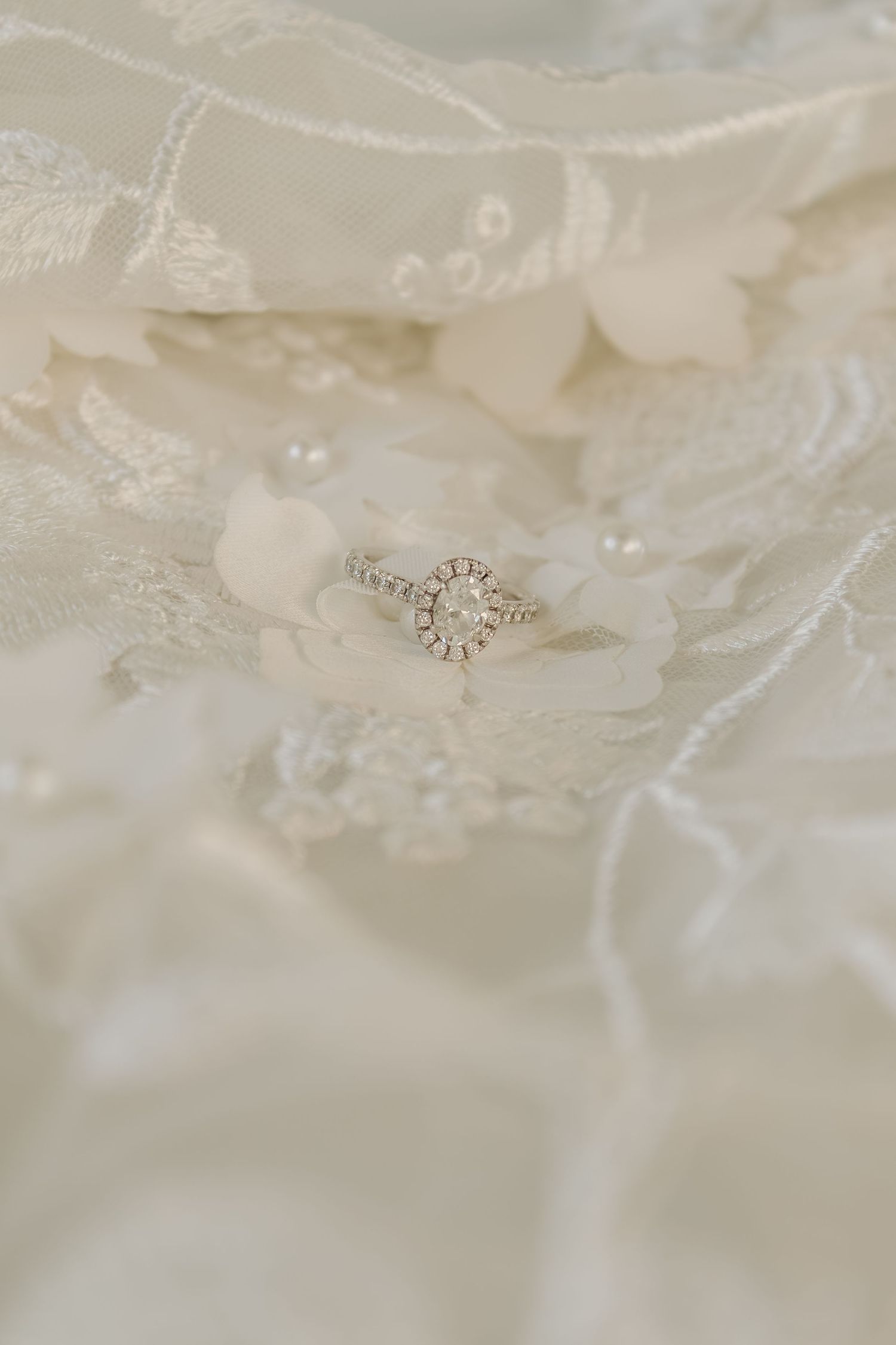 Delicate diamond ring photographed on intricate white lace wedding dress fabric.