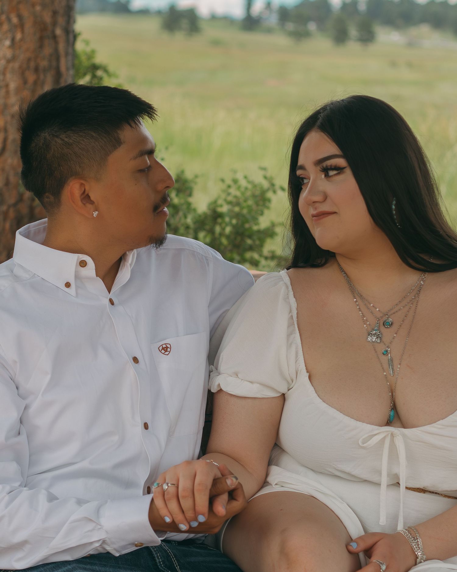 Intimate couple sitting close together outdoors in white outfits.