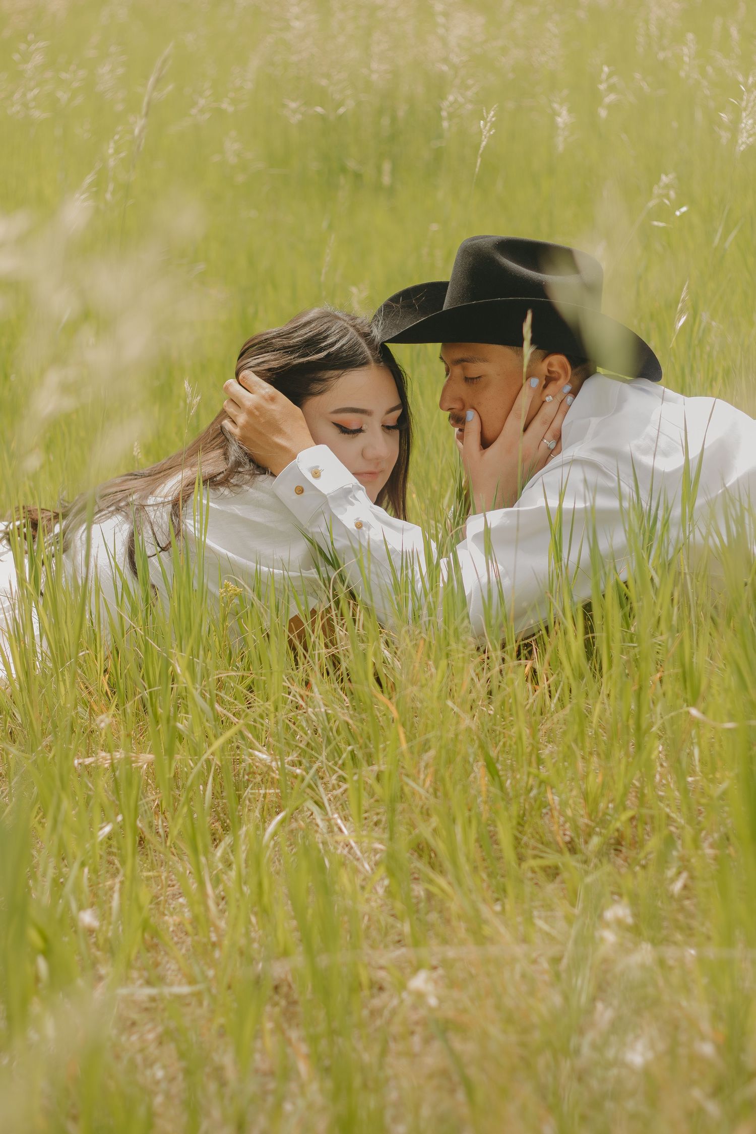 A tender moment between two people lying in tall grass on a sunny day.