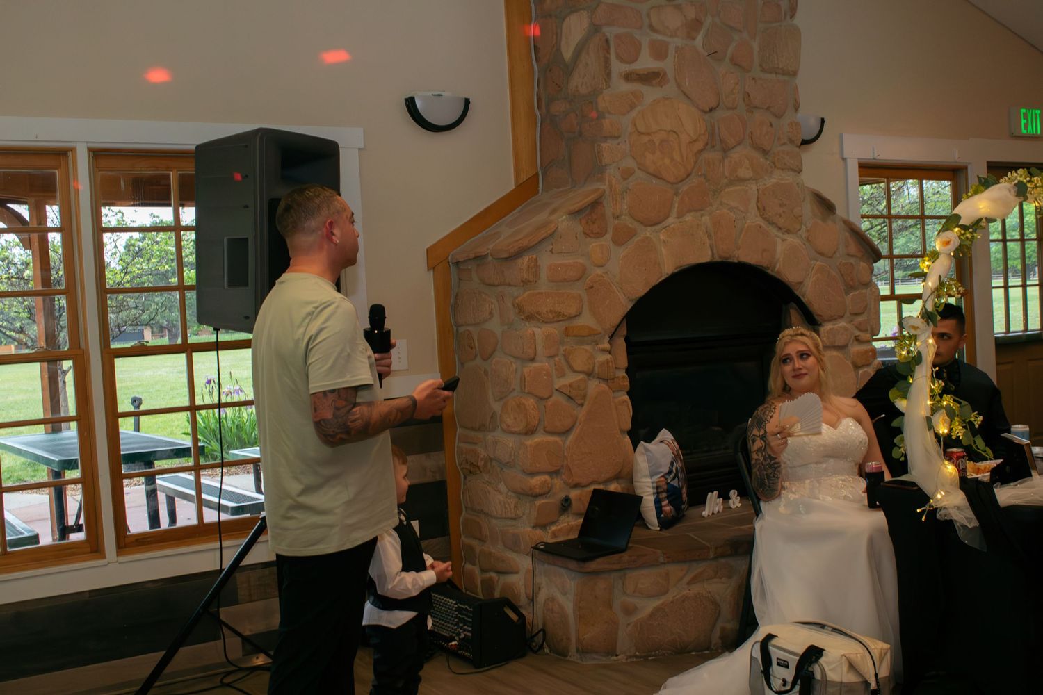 Wedding celebration in a rustic venue with stone fireplace and large windows overlooking green scenery.