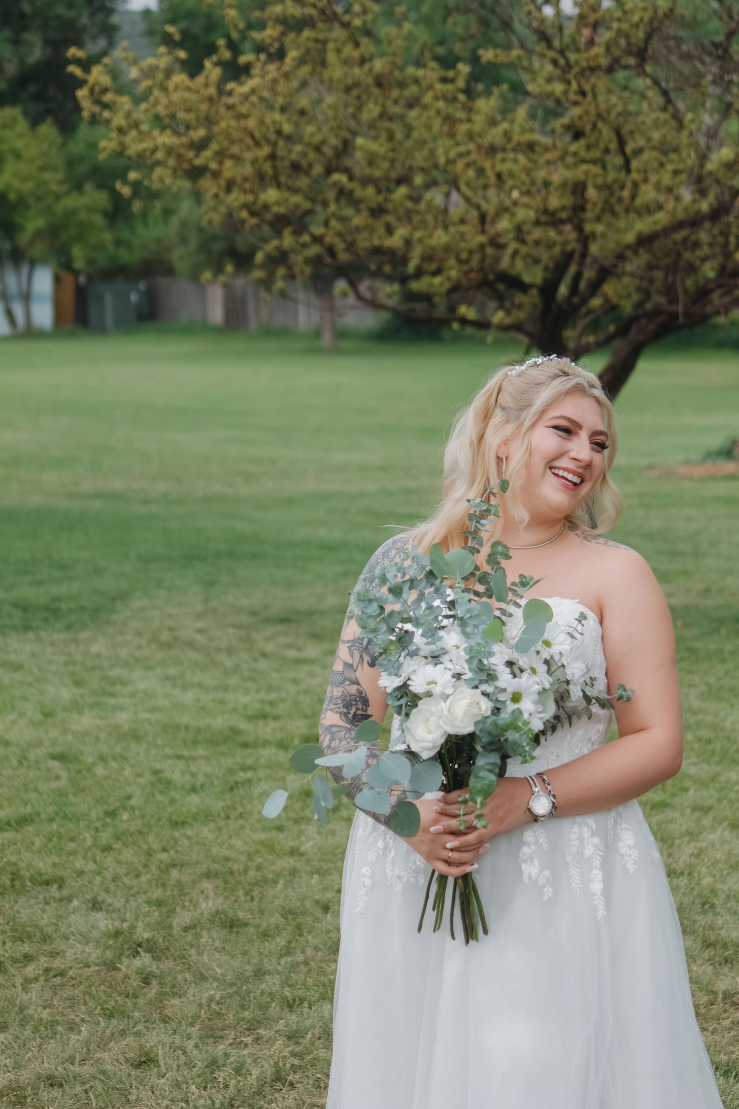 A bride in a white wedding dress holding a bouquet of white and green flowers outdoors.