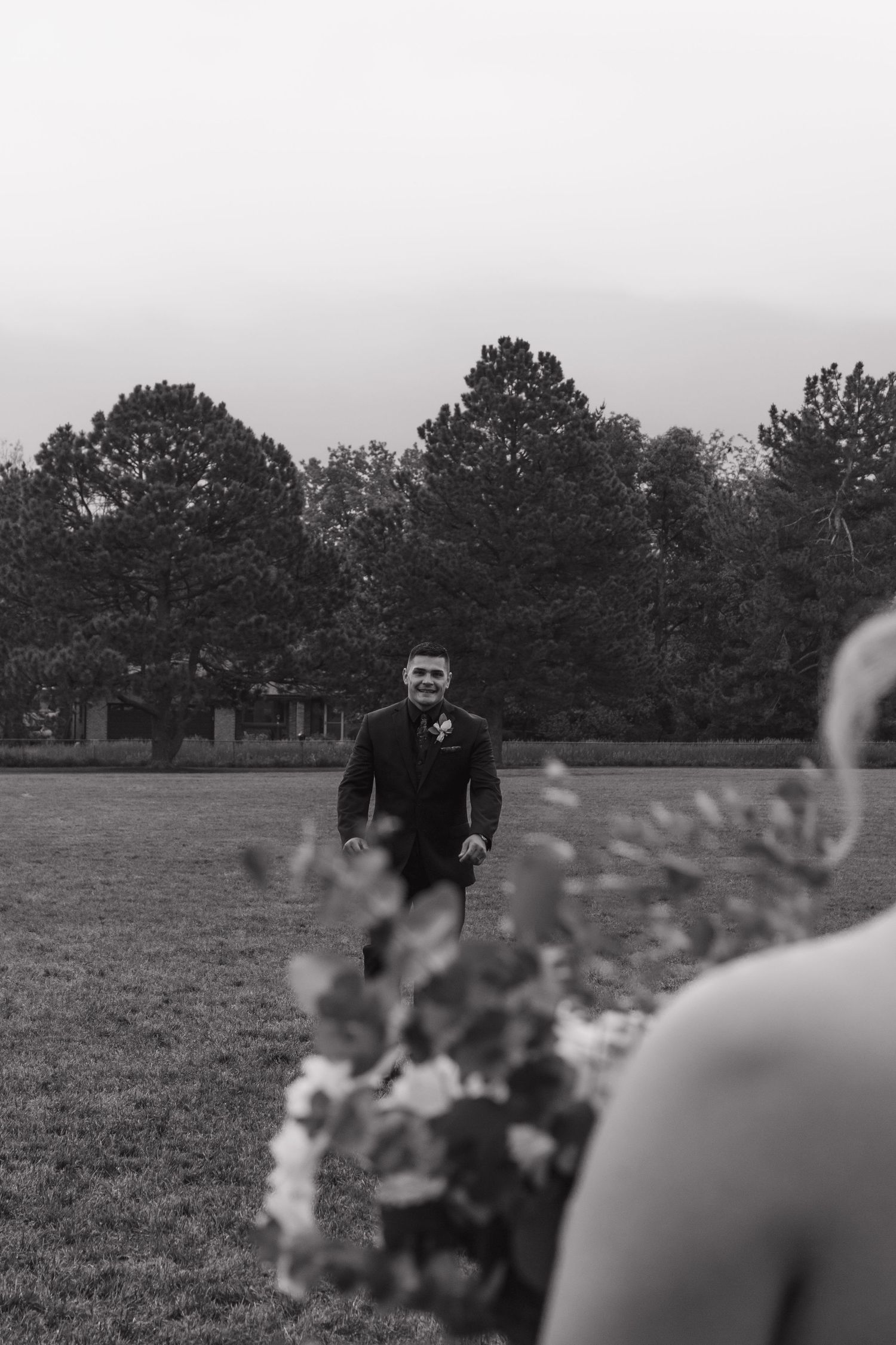 Black and white photo of groom anticipating first look in field with trees.